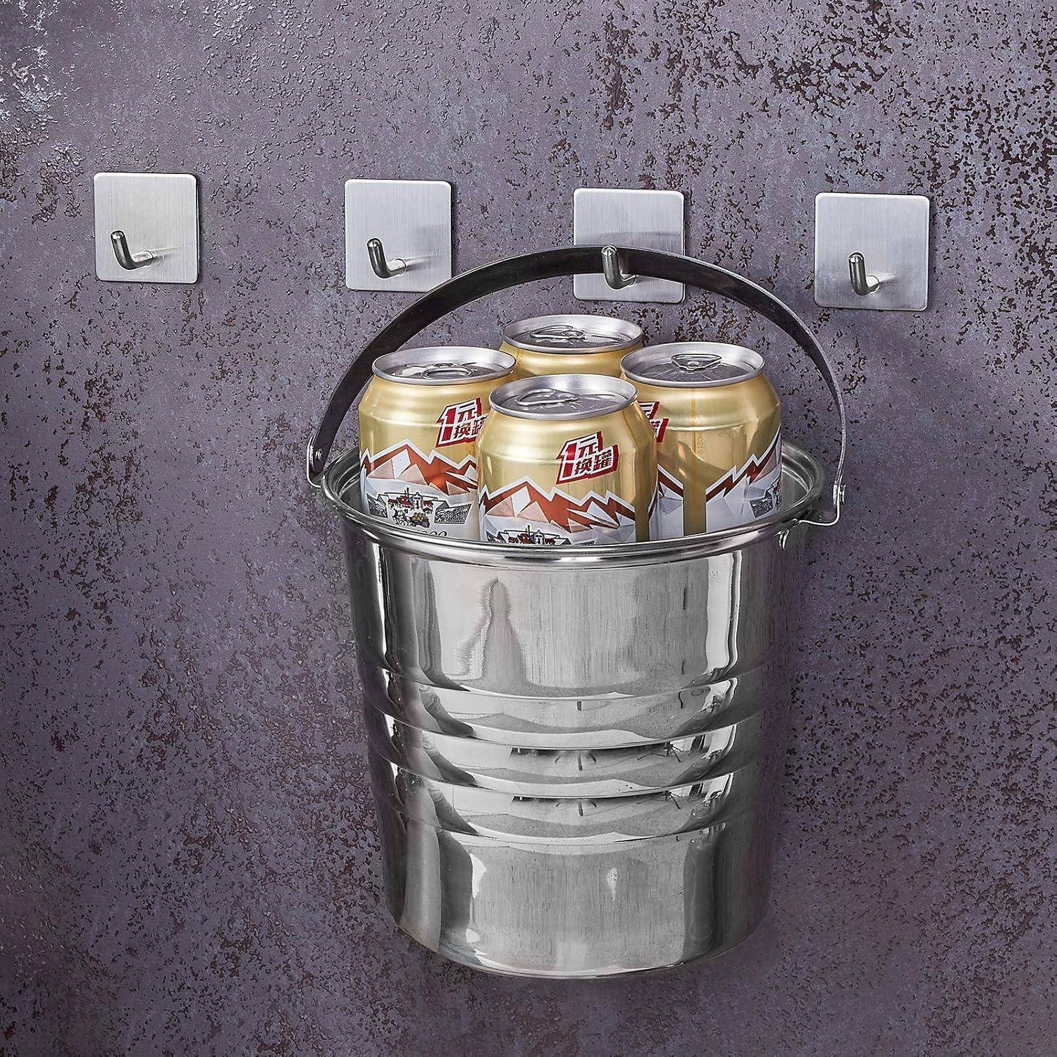 Ein glänzender Metallkübel, gefüllt mit ungeöffneten Dosen, hängt an einer Wand mit Haken und erzeugt vor der strukturierten Oberfläche einen rustikalen, industriellen Look.