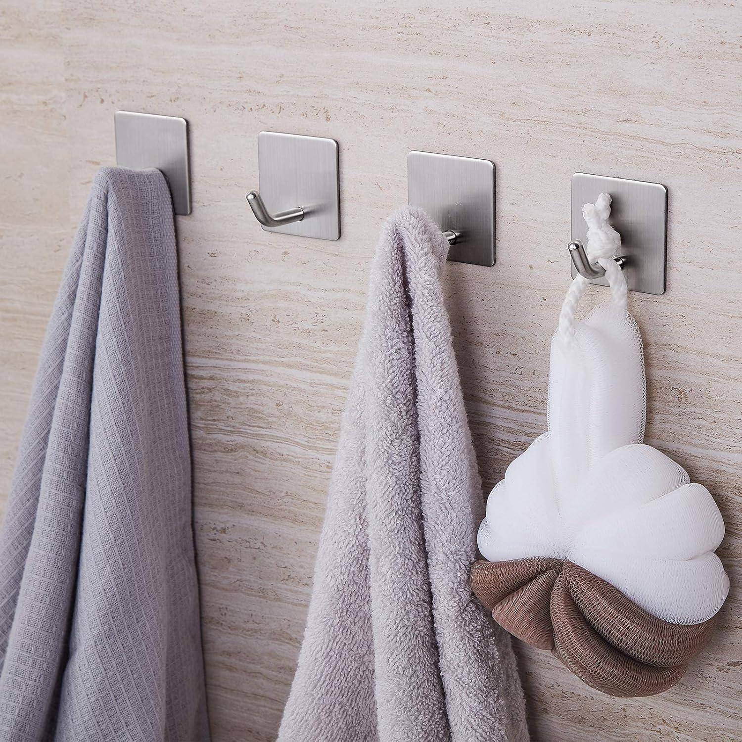 Handtücher und ein Loofa, die an Edelstahlhaken an einer gefliesten Wand hängen.