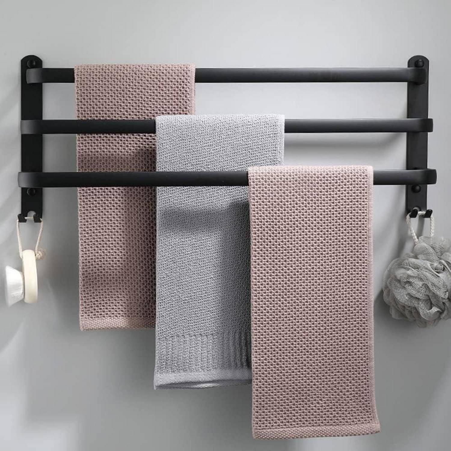 Drei Handtücher, zwei rosa und eines grau, hängen ordentlich an einem schwarzen Handtuchhalter vor einer hellgefärbten Wand, mit einem Badeschwamm, der in der Nähe hängt.