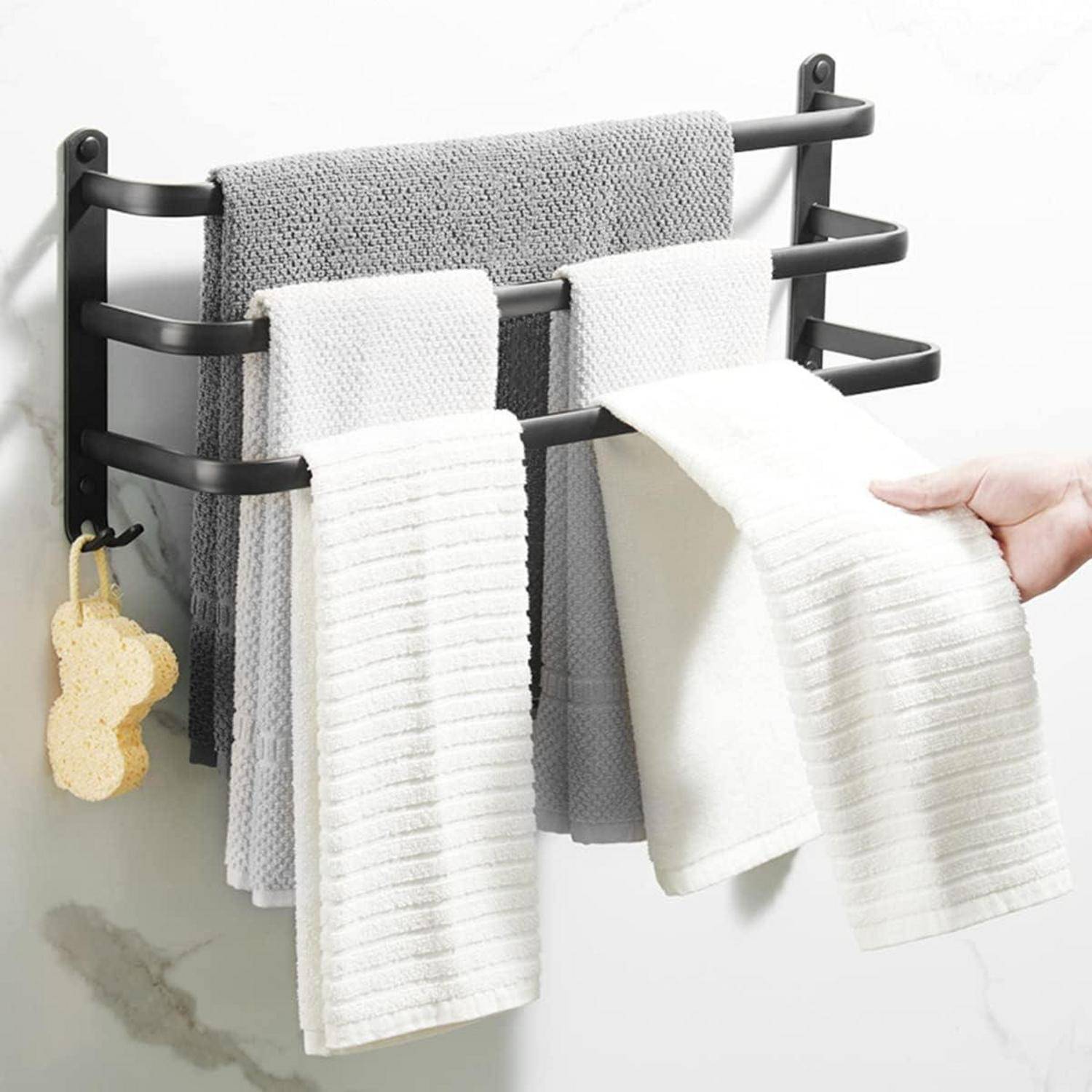 Ein schwarzes, wandmontiertes Handtuchgestell mit vier Armen hält verschiedene graue und weiße Handtücher. Eine Hand richtet ein Handtuch, während ein Schwamm darunter hängt.