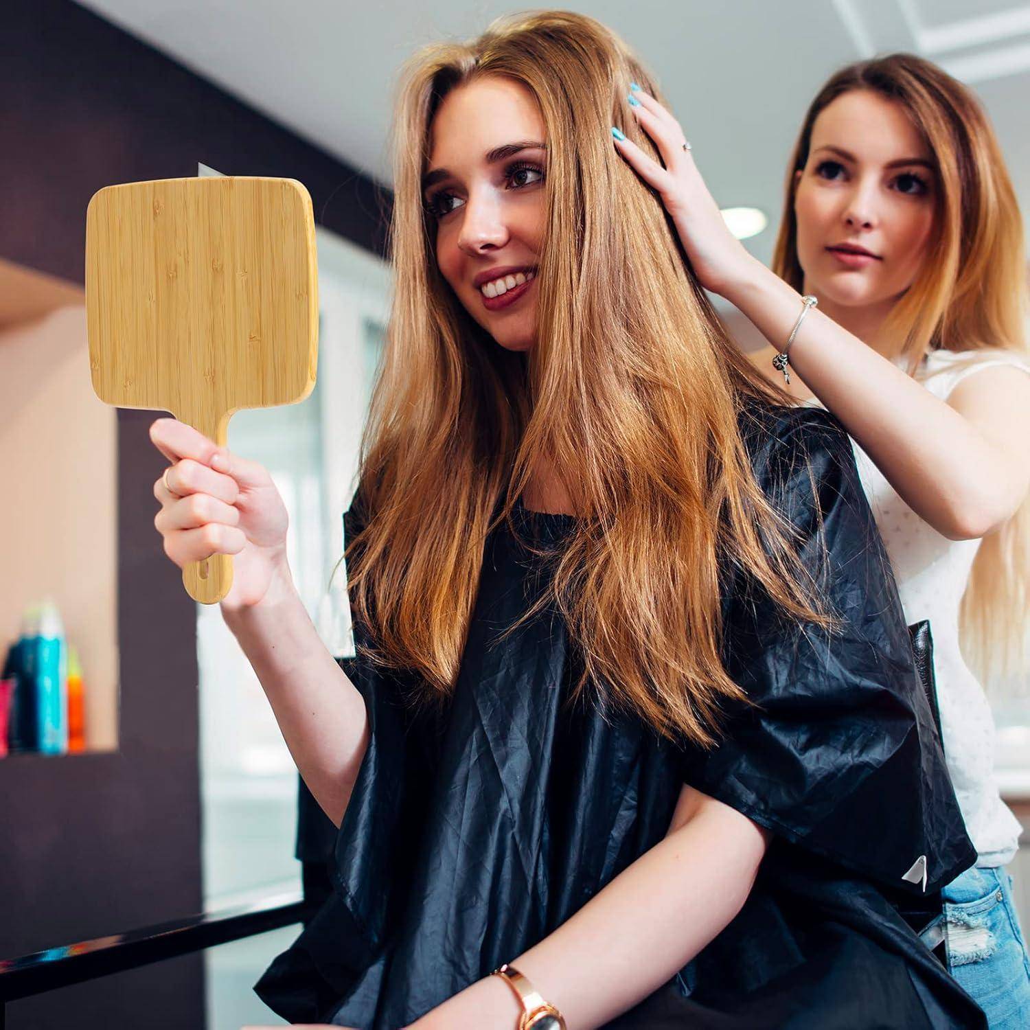 Eine Frau in einem Salon hält einen Handspiegel und bewundert ihre neue Frisur. Ein Friseur steht neben ihr und richtet ihr Haar.