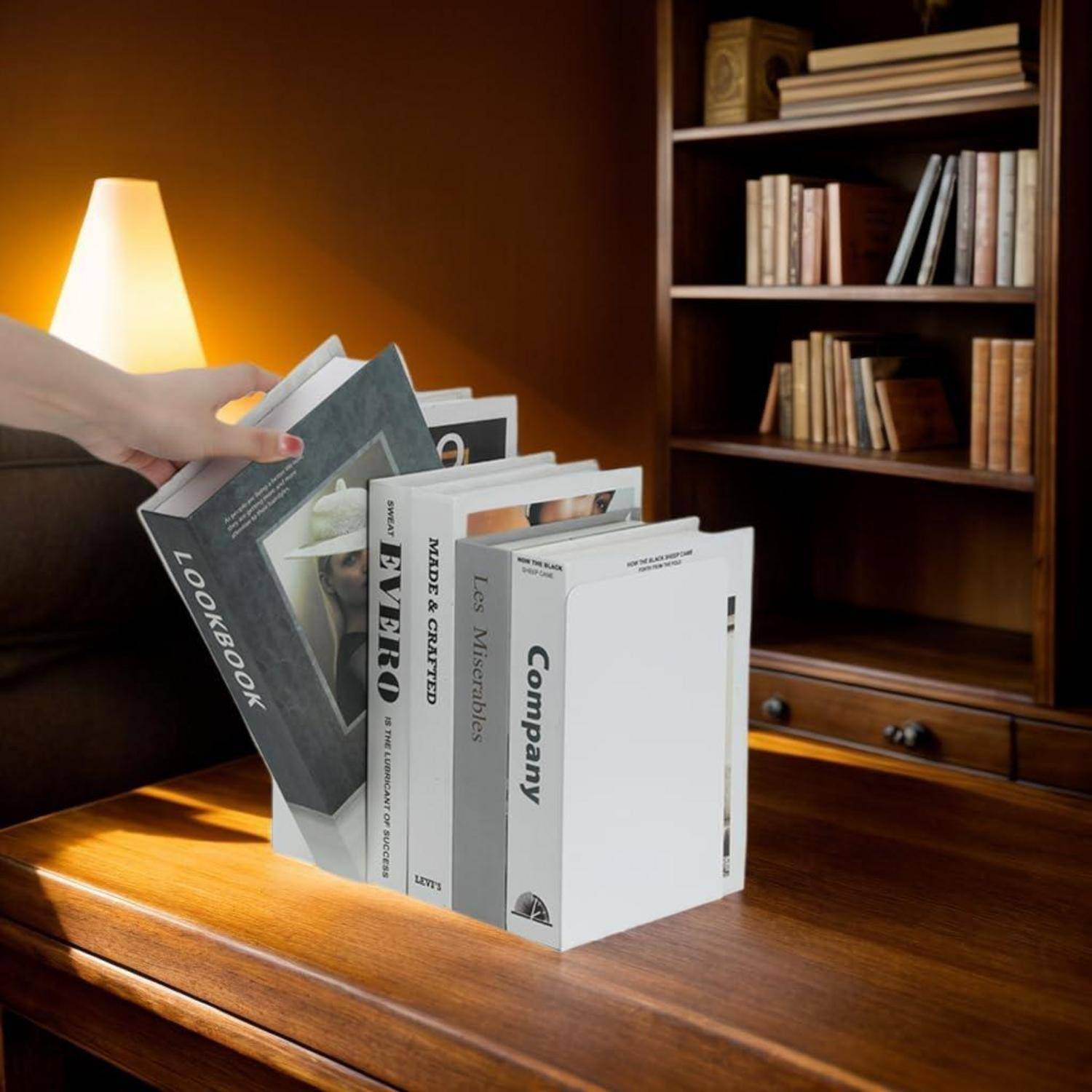 Eine Person legt ein Buch in einen minimalistischen Buchhalter auf einem Holztisch. Im Hintergrund sind Regale mit Büchern zu sehen.