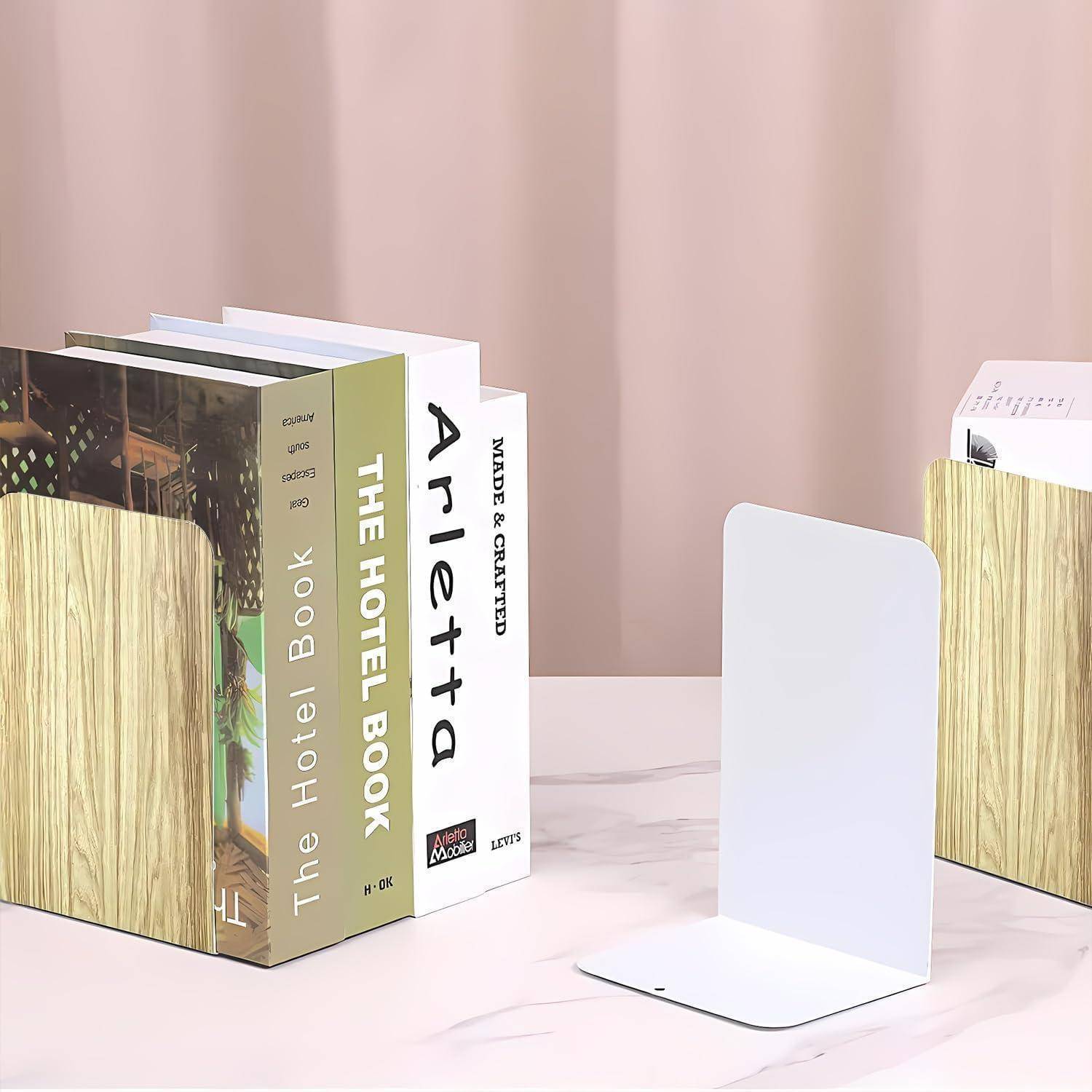 Bücher mit unterschiedlichen Buchrückendesigns sind sauber zwischen weißen Metallbuchstützen auf einer pastellrosa Oberfläche platziert.
