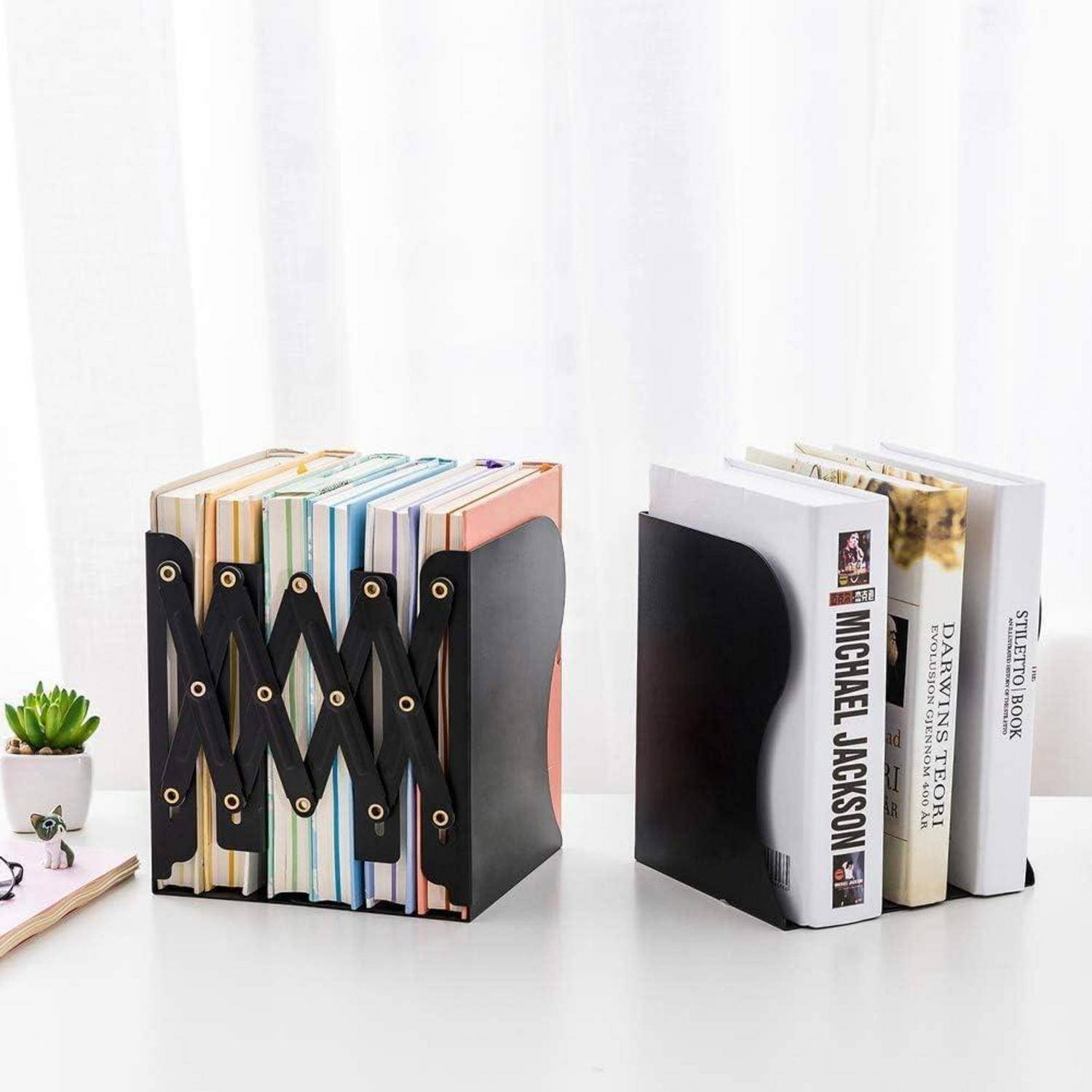 Verstellbare Buchstützen halten eine Reihe bunter Bücher, während Sonnenlicht durch transparente Gardinen hereinströmt. Eine kleine Pflanze und Gläser befinden sich in der Nähe.