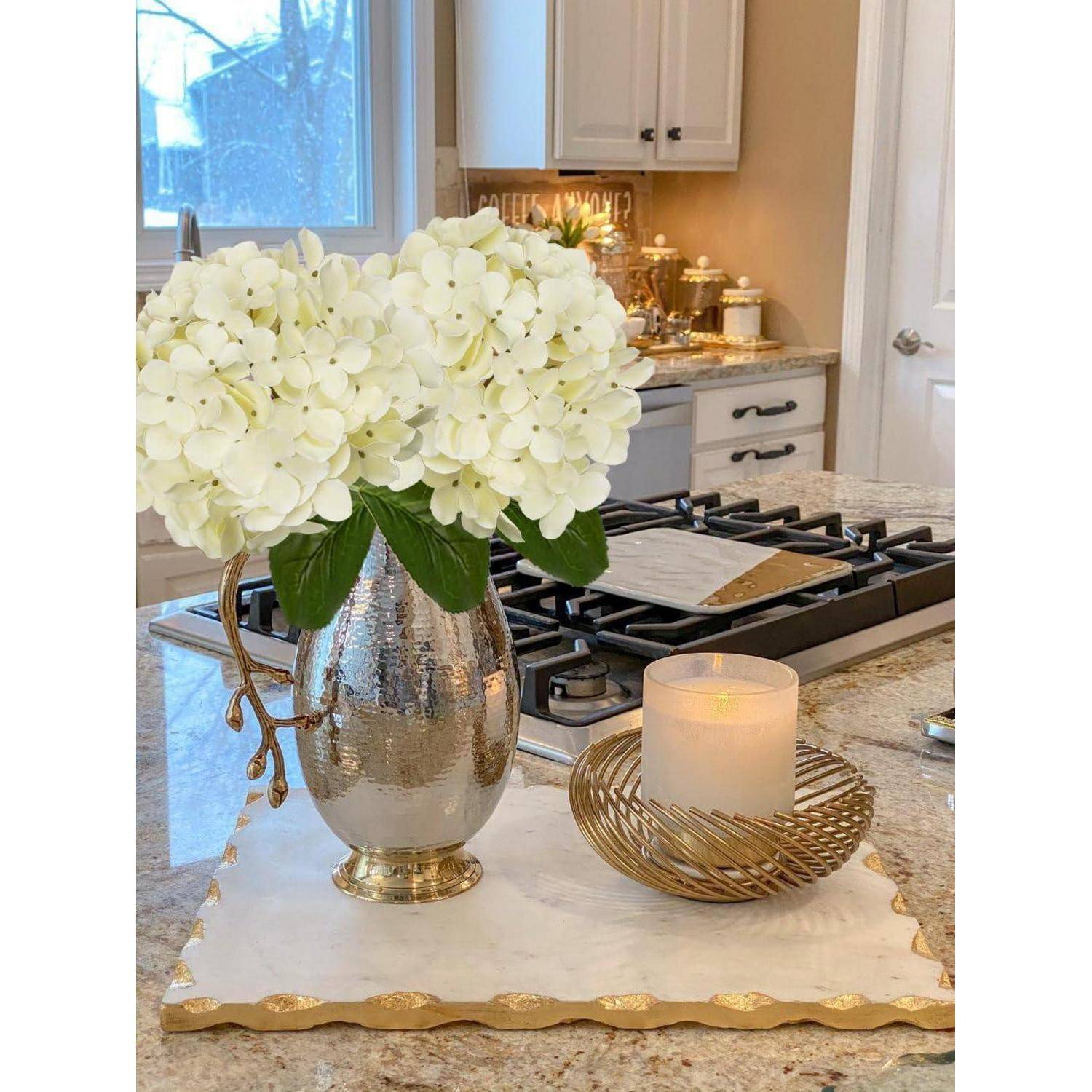 Eine Küche mit einer Marmorarbeitsplatte zeigt eine silberne Vase mit weißen Blumen und einer brennenden Kerze und bietet eine warme und elegante Atmosphäre.