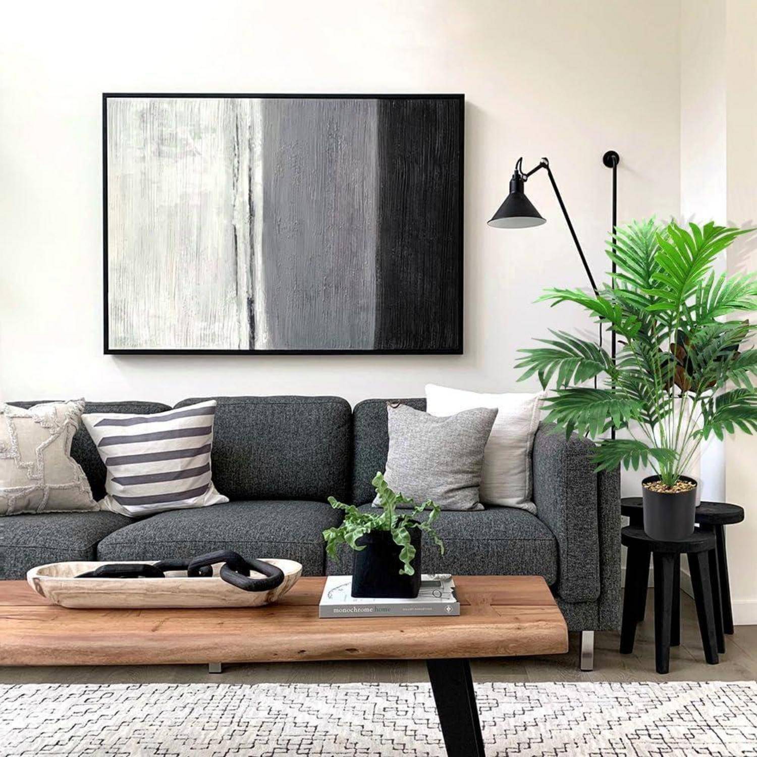 Ein modernes Wohnzimmer mit einem dunkelgrauen Sofa, gestreiften Kissen, einem Holzcouchtisch, einer Topfpflanze und abstrakter Wandkunst.
