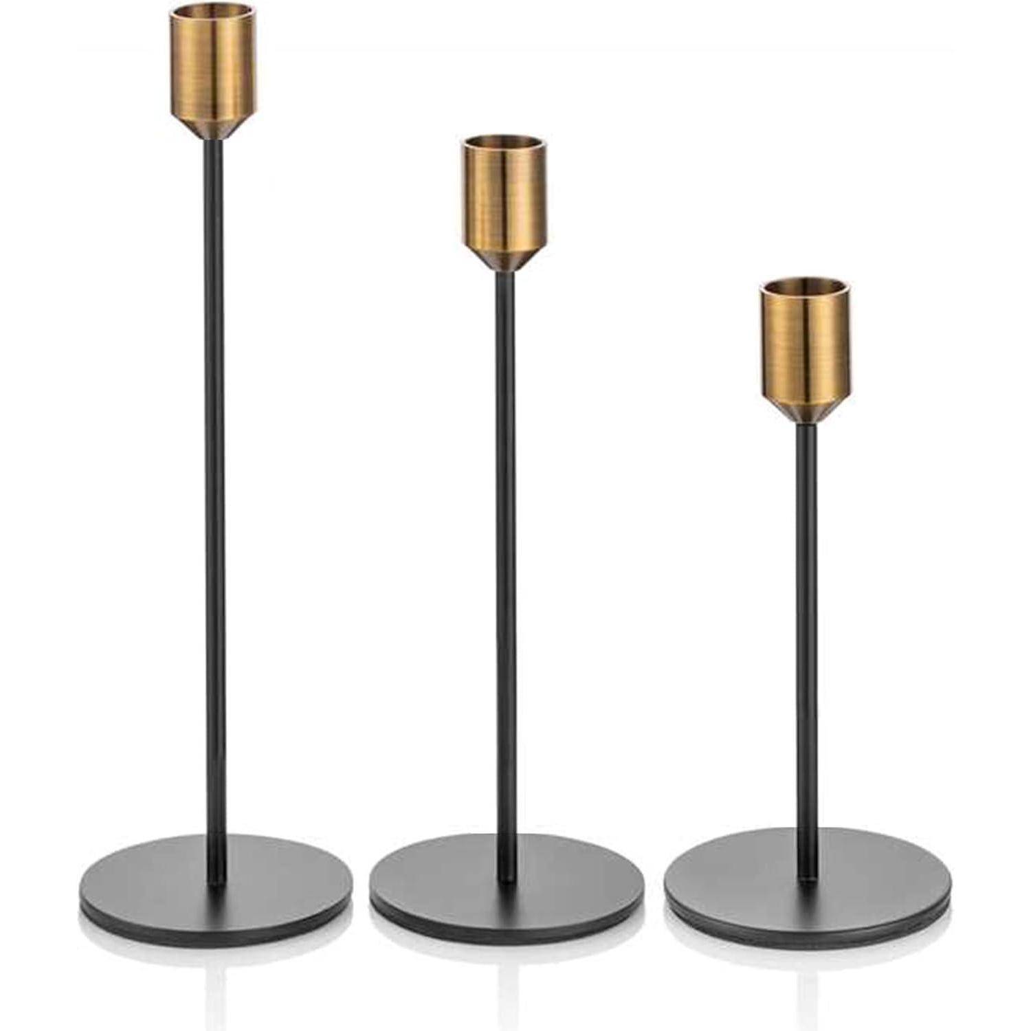 Drei zylindrische Bronzekerzenhalter auf schwarzen Metallstängeln und kreisförmigen Basen, in der Höhe von größter zu kleinster abgestuft.