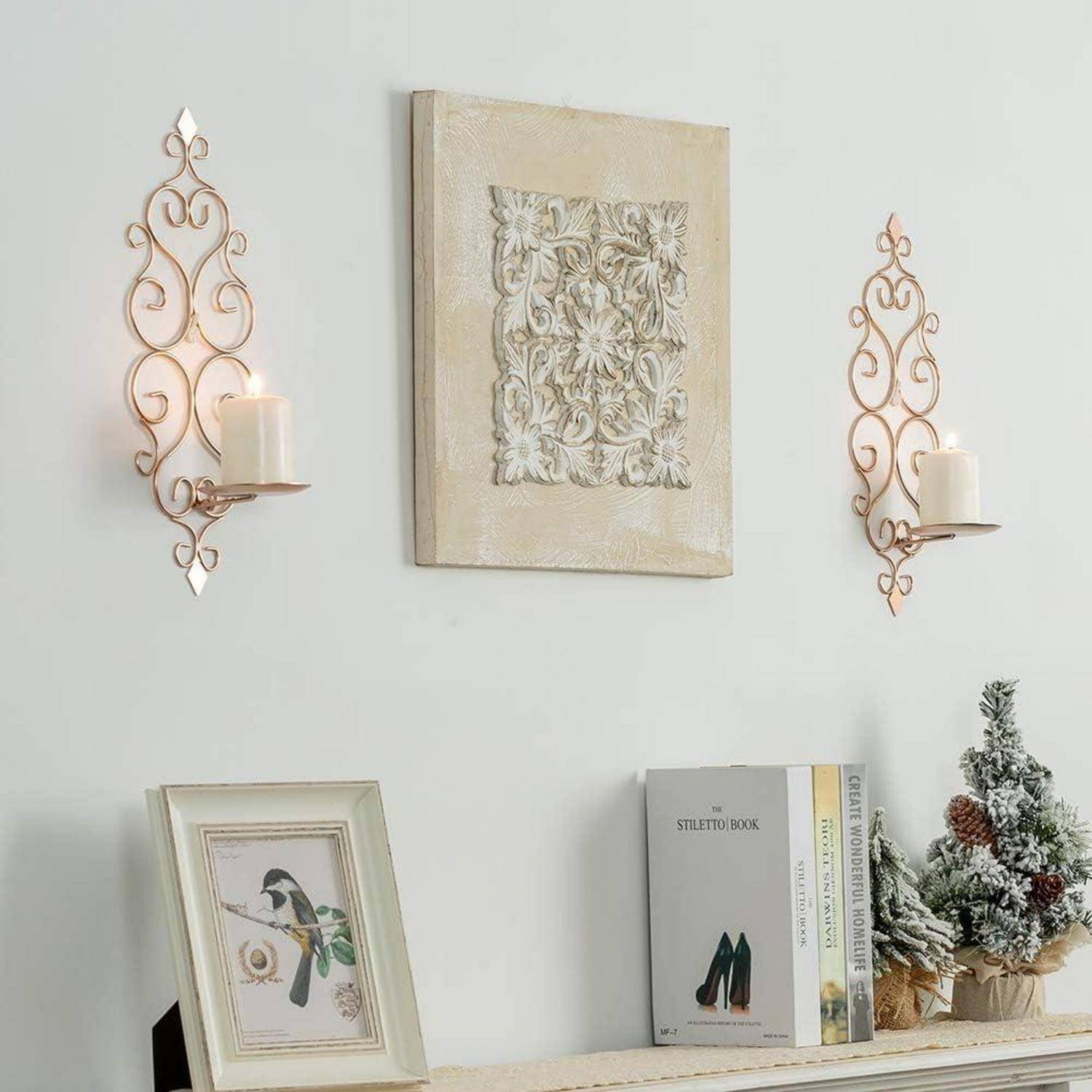 Eine Wanddekoration mit kunstvollen Kerzenhaltern, einem floralen Reliefpaneel und einem kleinen Regal mit gerahmten Kunstwerken und dekorativen Büchern.