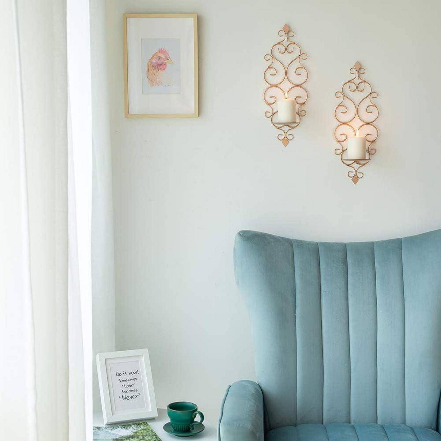 Ein blau gepolsterter Stuhl steht in der Nähe eines Fensters mit transparenten Vorhängen. Darüber befinden sich zwei verzierte Wandleuchter mit Kerzen und ein Blumenbild.