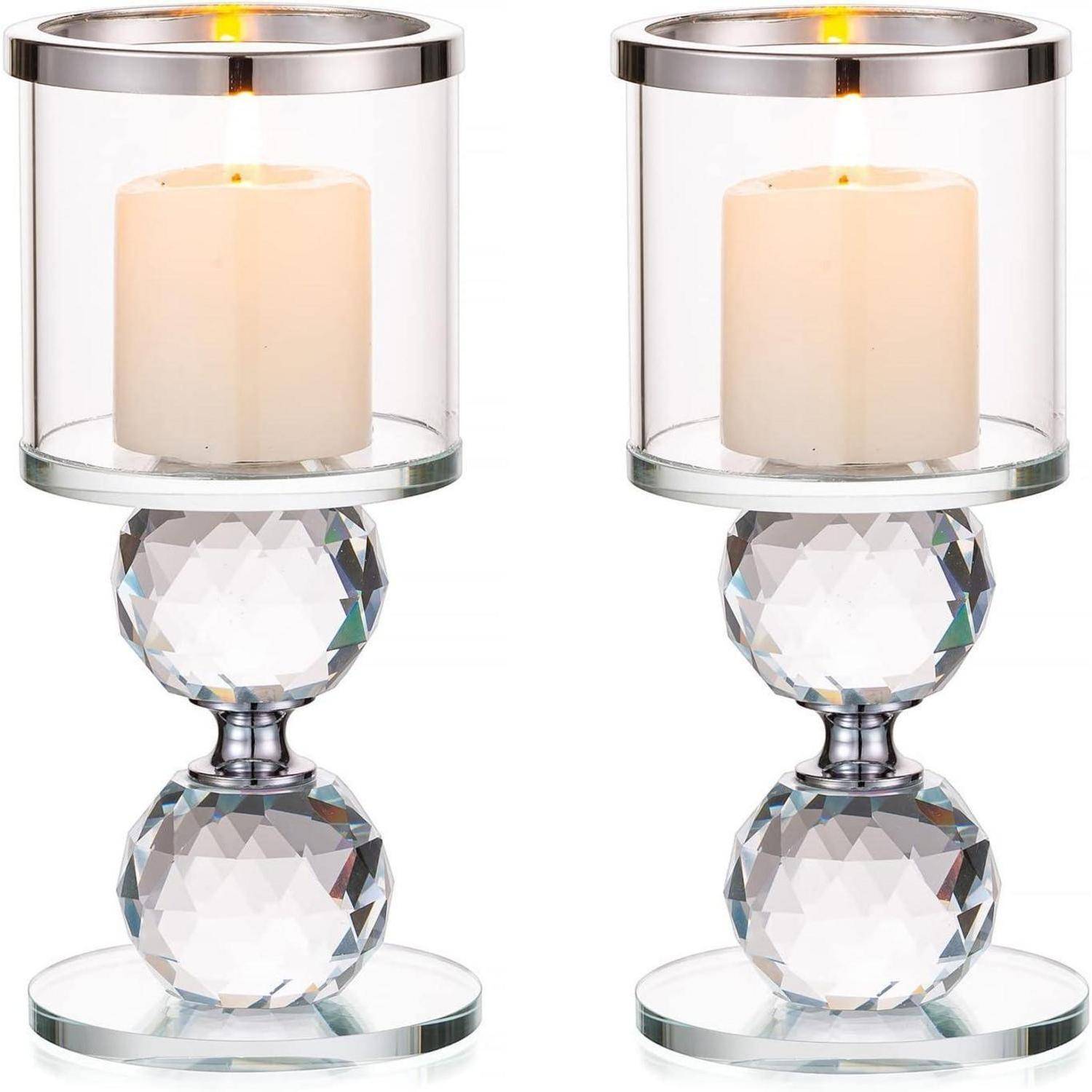 Zwei Kerzenhalter aus Glas mit weißen Kerzen, die ein kugelförmiges Kristalldesign in der Mitte und eine reflektierende Basis aufweisen und ein warmes Glühen ausstrahlen.
