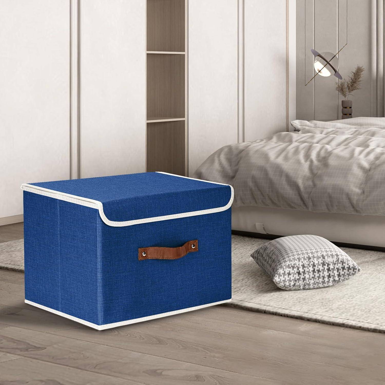 Eine blaue Aufbewahrungsbox mit einem Ledergriff steht auf einem Holzboden. Ein Bett und Kissen sind im Hintergrund zu sehen, was auf eine Schlafzimmerumgebung hindeutet.