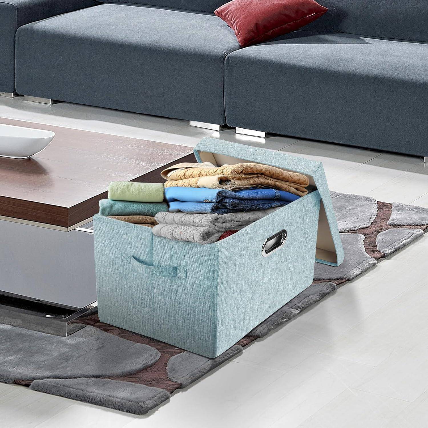 Eine blaue Aufbewahrungsbox, gefüllt mit ordentlich gefalteten Kleidungsstücken, steht auf einem eleganten grau-weißen gemusterten Teppich neben einem Holzkaffeetisch.