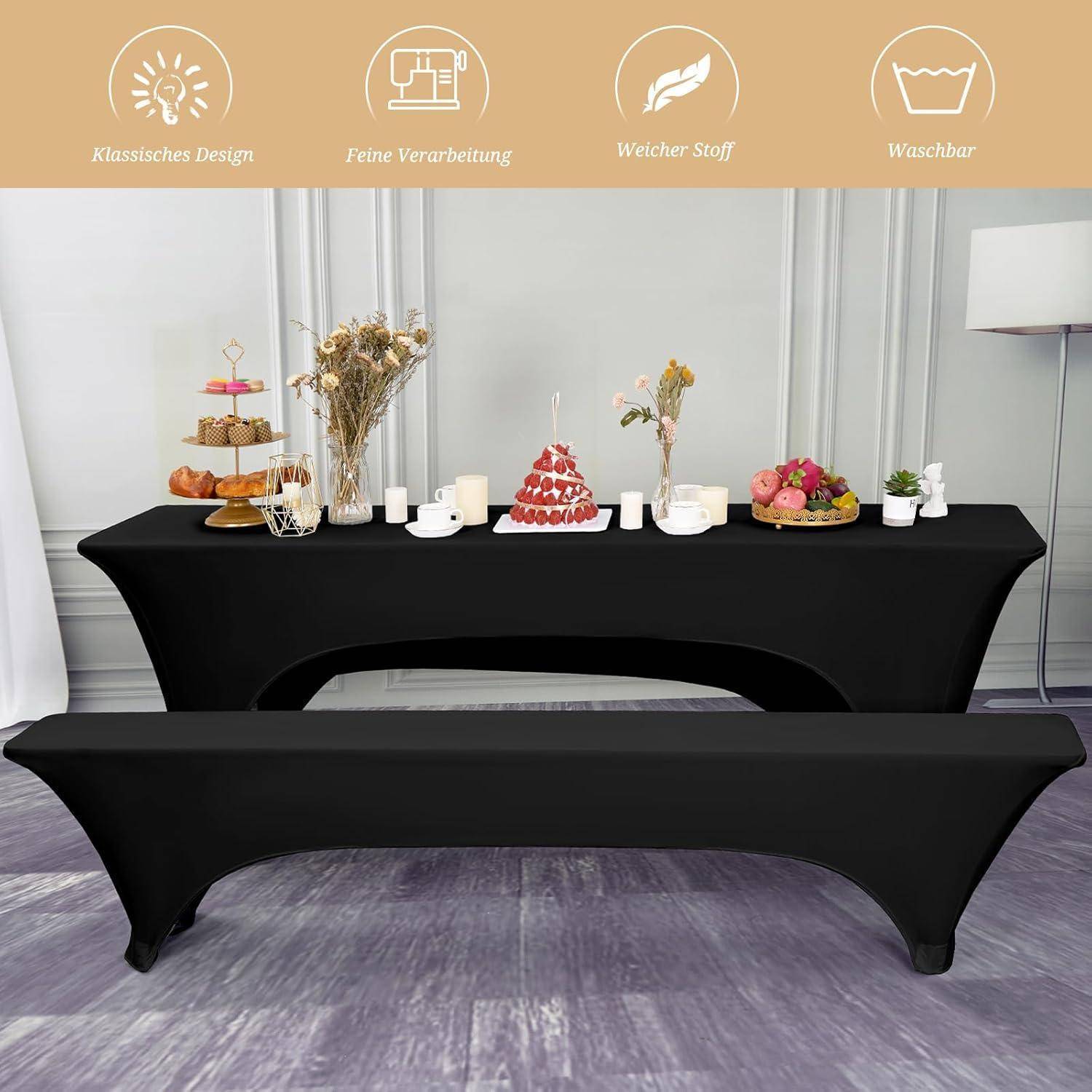 Ein Esstisch, der mit einer schwarzen Tischdecke gedeckt ist, mit einem mehrstufigen Dessertständer, einem Strauß getrockneter Blumen, einem roten Kuchen und einigen kleinen Schalen. Weiße Wände und eine Lampe im Hintergrund.