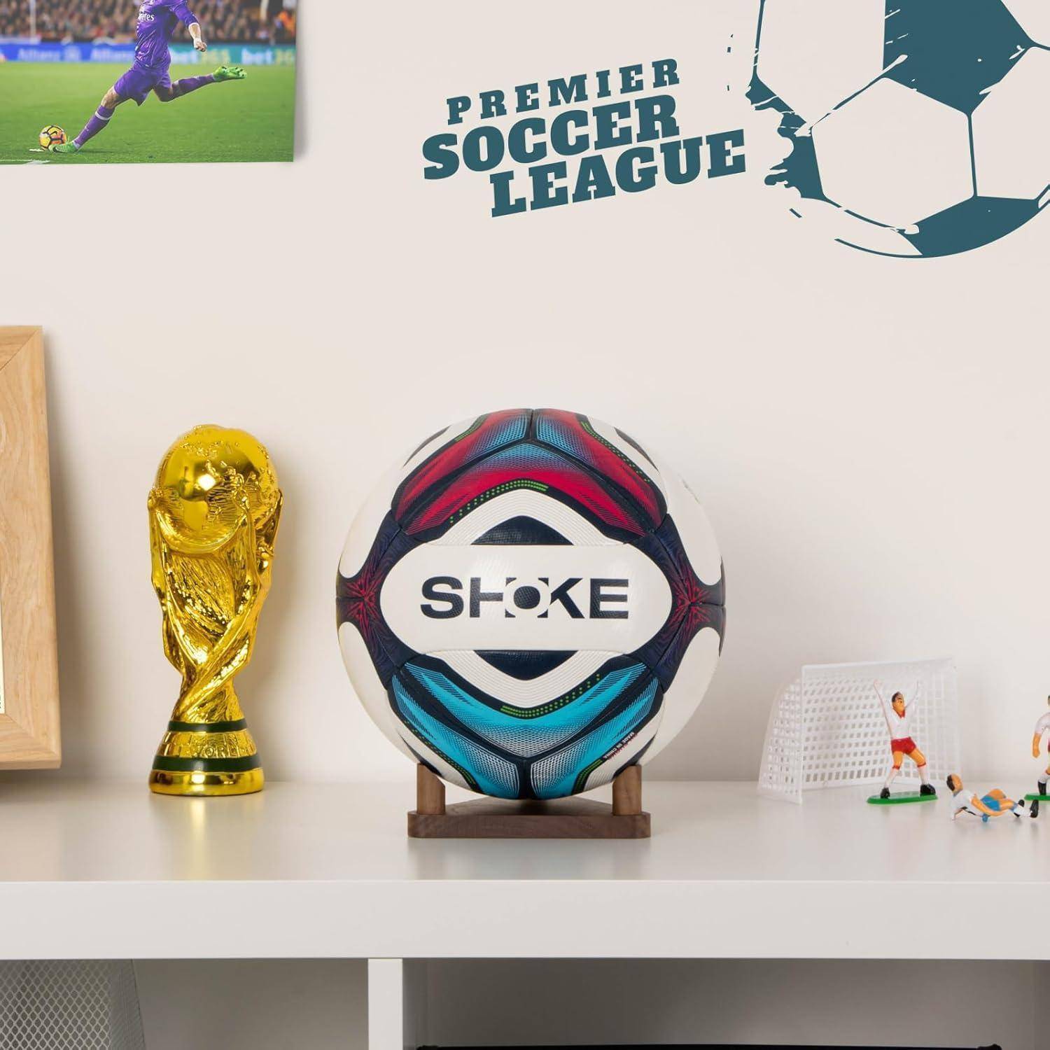 Ein Regal zeigt eine Nachbildung des Weltmeisterschaftspokals, einen Fußball mit der Beschriftung ‚Premiere Soccer League' und kleine Fußballspieler-Figuren.