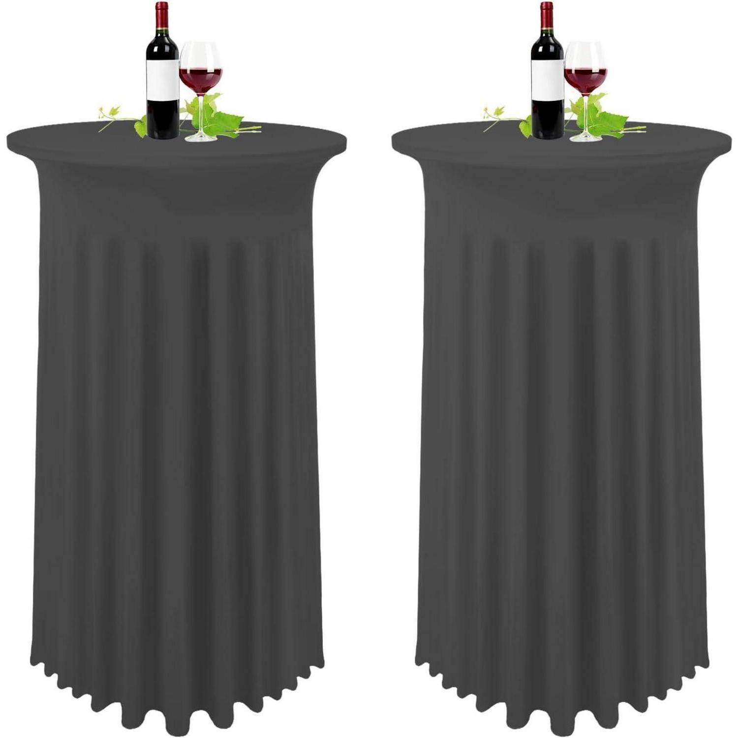 Zwei hohe Tische mit schwarzen Tischdecken, auf denen jeweils eine Weinflasche, ein gefülltes Weinglas und grüne Blätter zur Dekoration stehen.