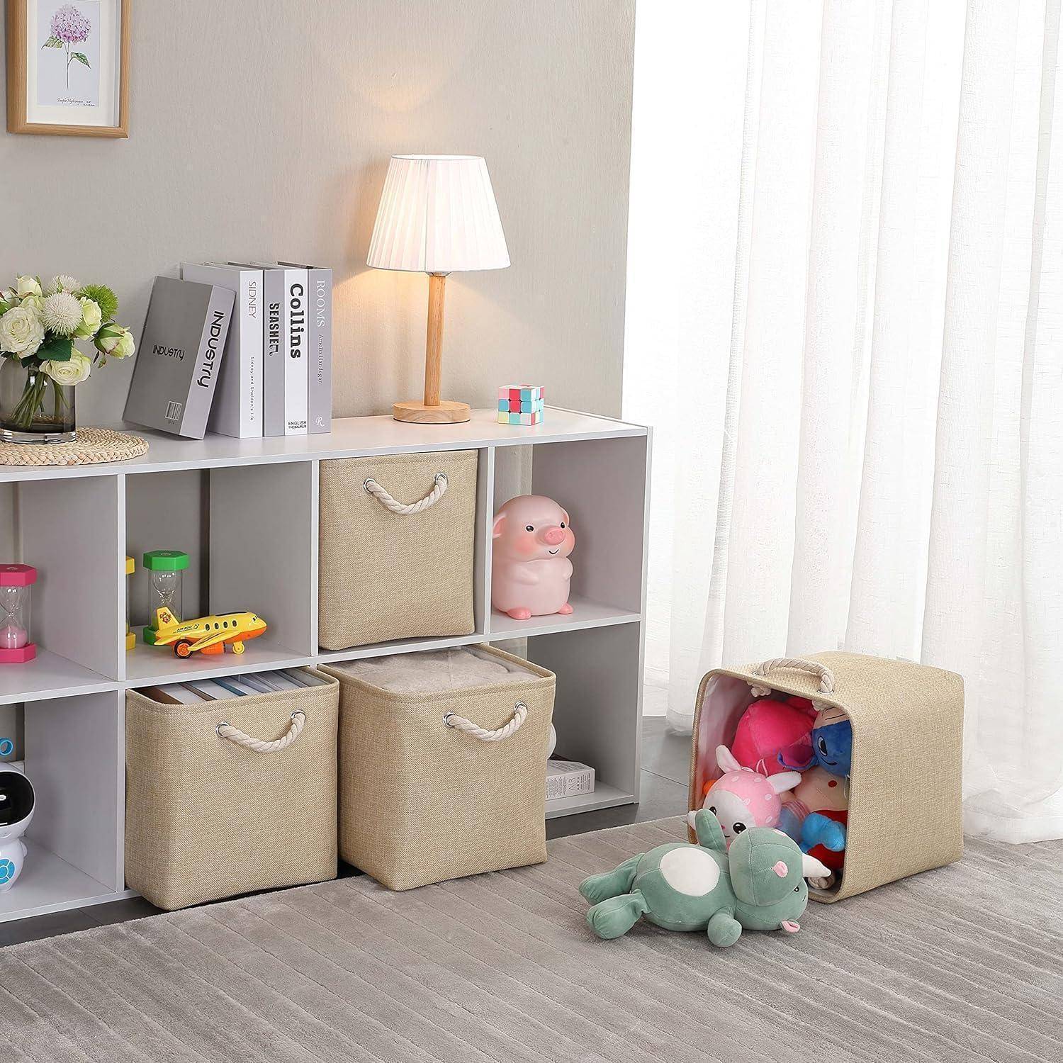 Ein aufgeräumter Kinderspielraum mit einem weißen Würfelregal, Plüschtieren und Büchern. Beige Aufbewahrungsboxen halten die Spielsachen. Eine Lampe und eine Pflanze stehen obenauf.