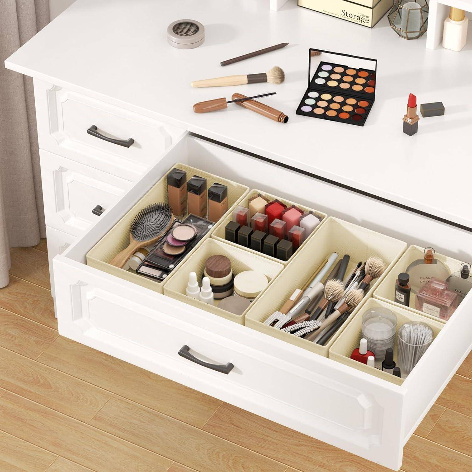 Ein weißer Schminktisch mit Make-up und Pinseln auf der Oberfläche, offene Schublade darunter mit ordentlich sortierten Kosmetika und Beautyprodukten.