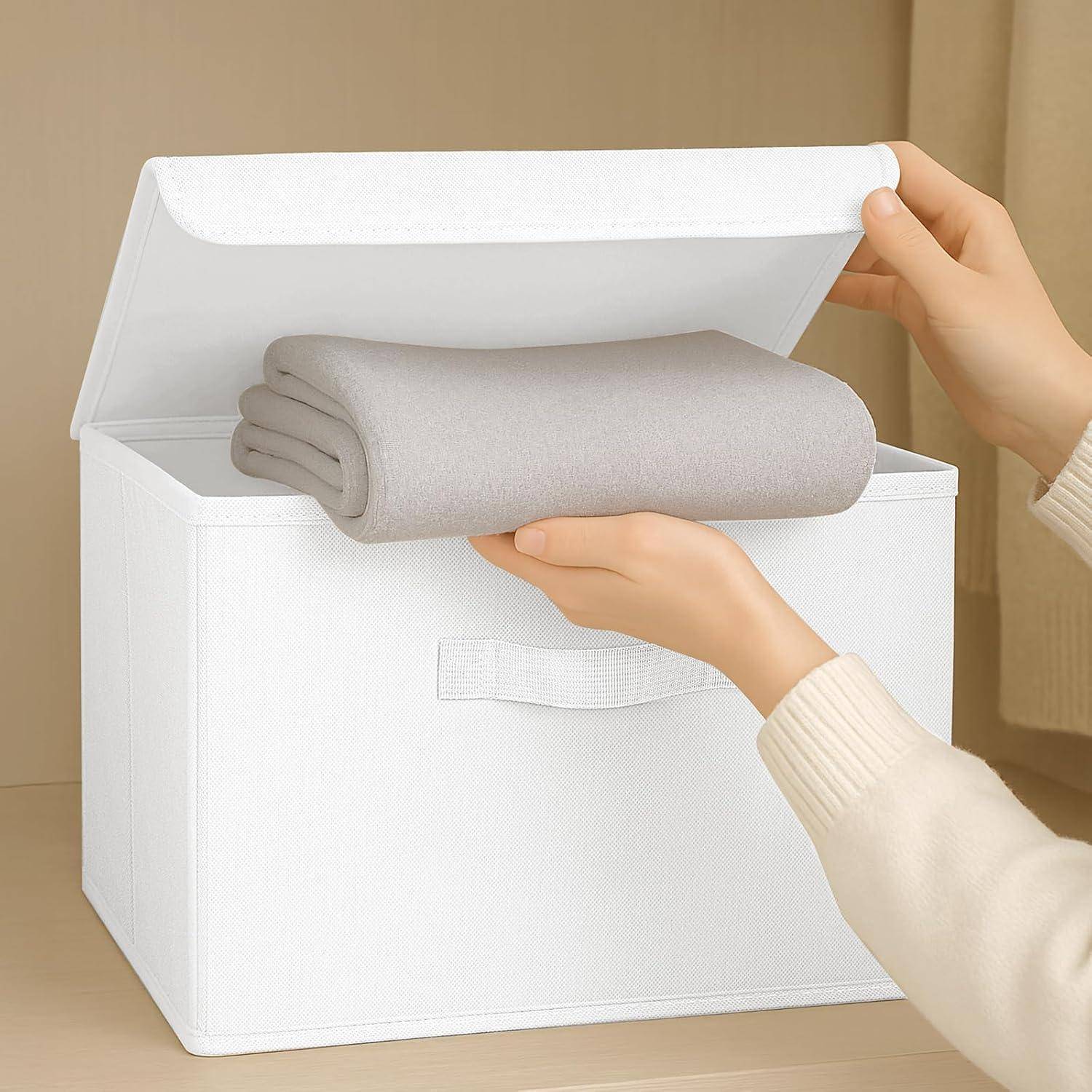Eine Person legt ein zusammengefaltetes graues Handtuch in eine weiße Aufbewahrungsbox mit Deckel. Die Szene deutet auf Organisieren oder Aufräumen hin.