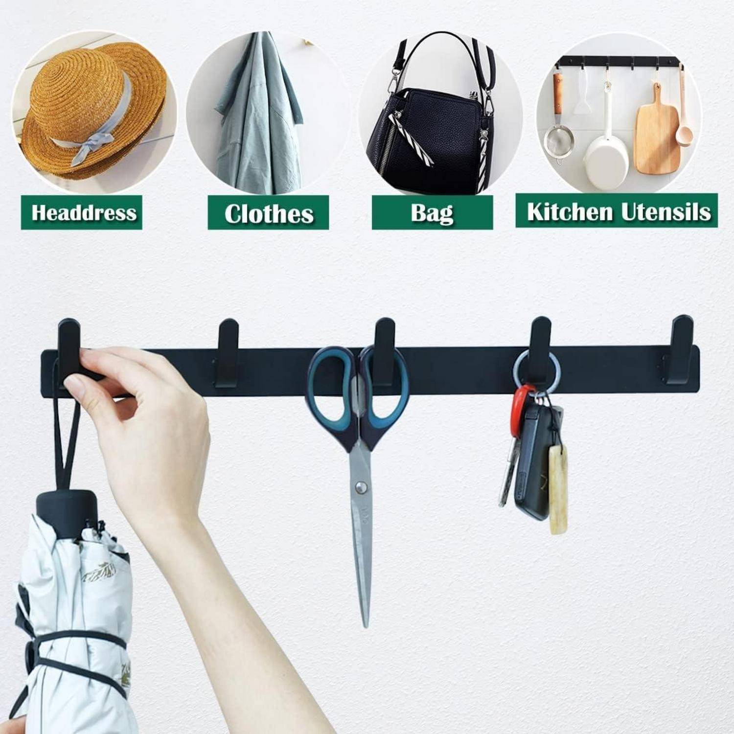 Ein an der Wand montierter Haken-Halter mit verschiedenen Gegenständen: ein Regenschirm, eine Schere, ein Schlüsselring. Darüber Schilder, die Verwendungszwecke angeben: 'Kopfbedeckung', 'Kleidung', 'Tasche', 'Küchenutensilien'.