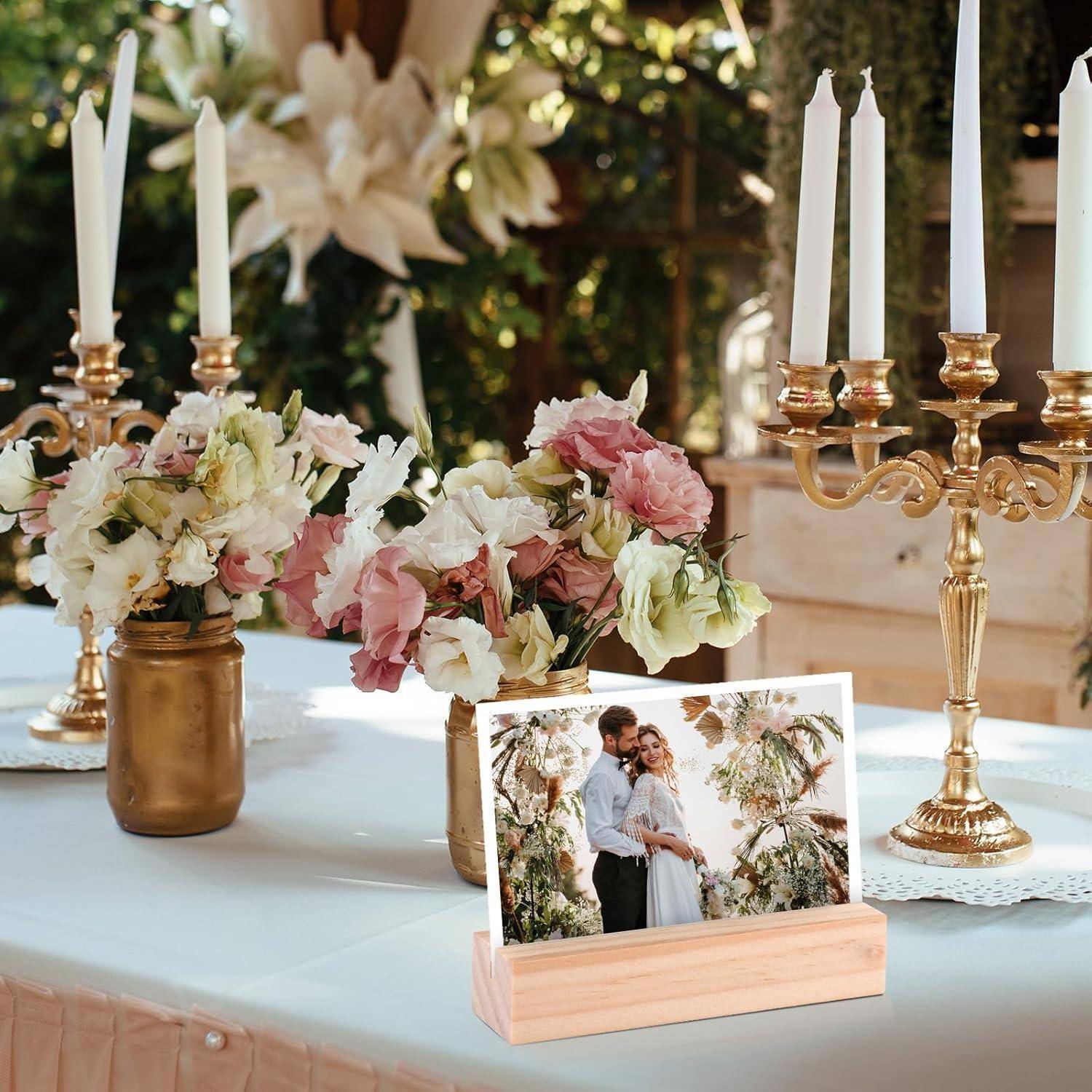 Ein geschmückter Hochzeitstisch mit Blumenarrangements, goldenen Kerzenhaltern und einem gerahmten Foto eines sich umarmenden Paares inmitten von Grünpflanzen und Blumen.
