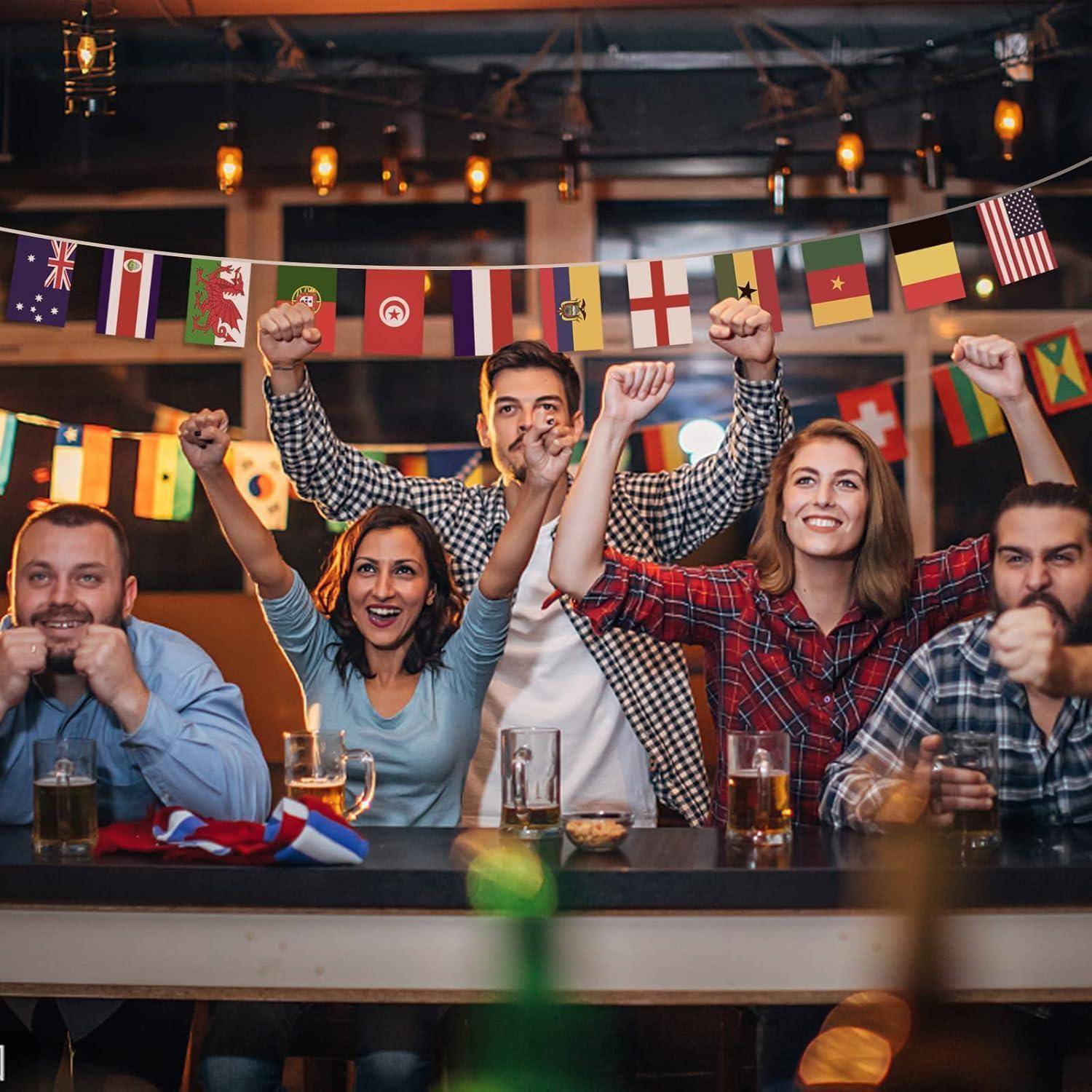 Eine Gruppe fröhlicher Menschen feiert, während sie eine Sportveranstaltung verfolgt, umgeben von verschiedenen internationalen Flaggen. Jeder von ihnen hält ein Getränk.