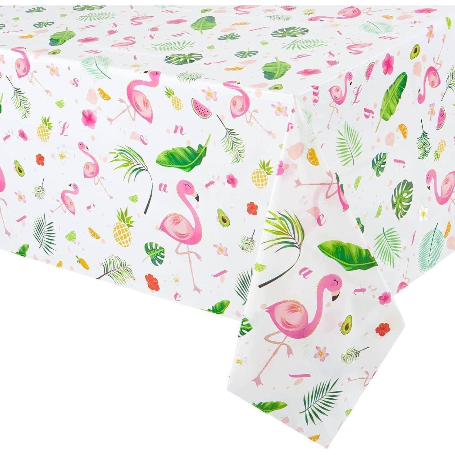 Ein Tisch, der mit einer weißen Tischdecke bedeckt ist, die bunte Drucke von Flamingos, Ananas, Blättern und tropischen Elementen zeigt.