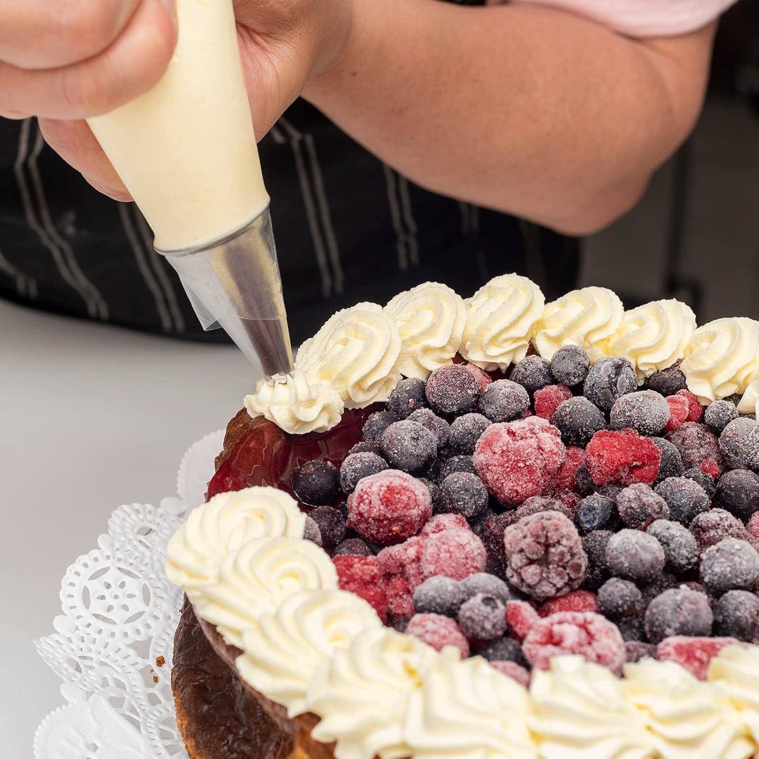 Eine Person verziert einen Kuchen, der mit verschiedenen gefrorenen Beeren belegt ist, und verwendet dabei einen mit Sahne gefüllten Spritzbeutel.