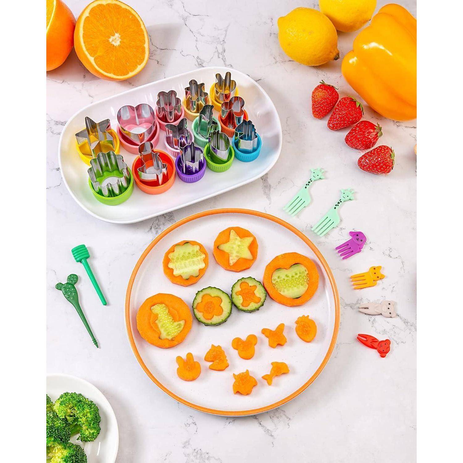 Verschiedene Obst- und Gemüsesorten sind auf einem weißen Teller in spielerische Formen geschnitten. Bunte Ausstecher und ganze Früchte umgeben den Teller.