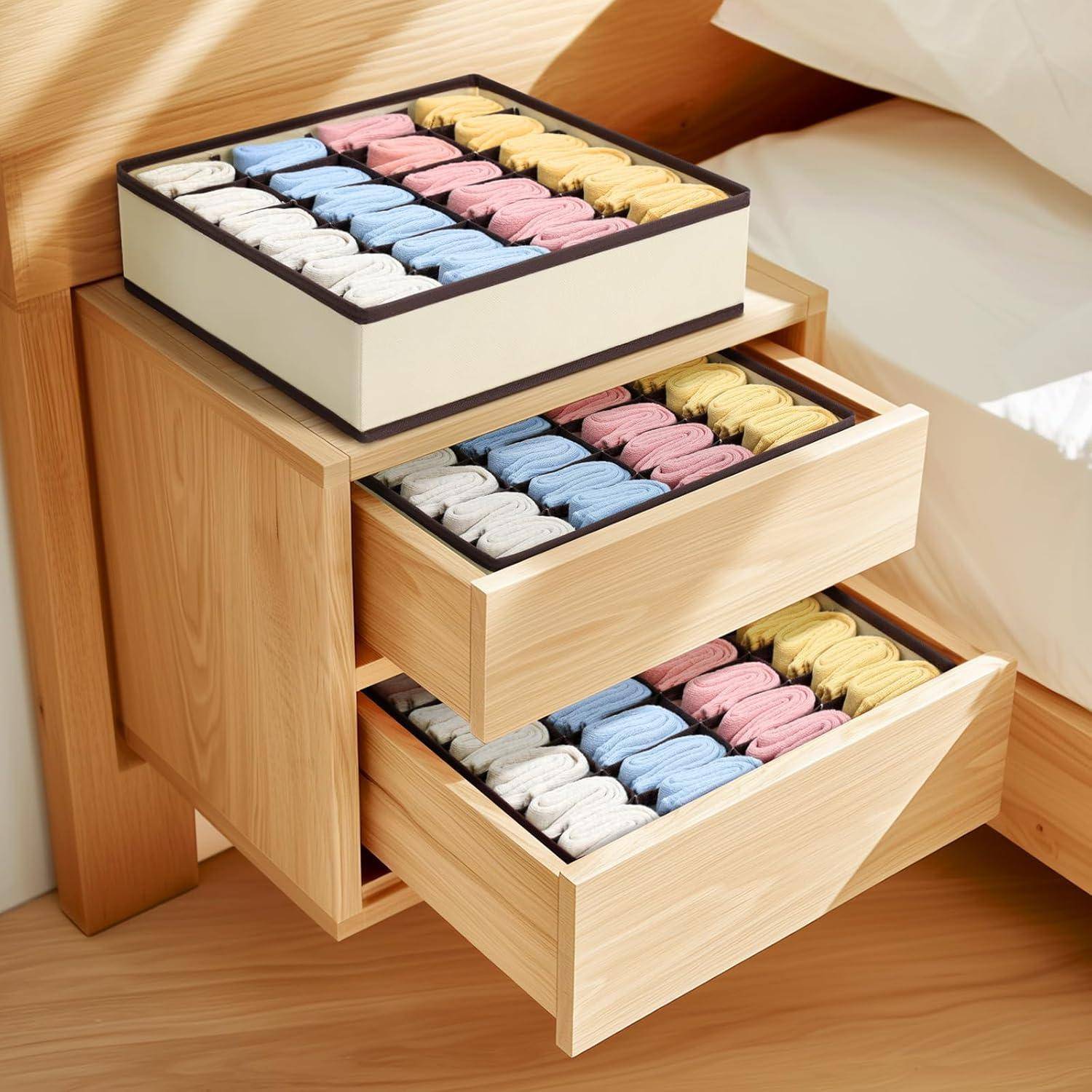 Ein Holz-Nachttisch mit zwei offenen Schubladen, die jeweils ordentlich mit gefalteten Kleidungsstücken in vier Farben sortiert sind: Beige, Blau, Rosa und Gelb.
