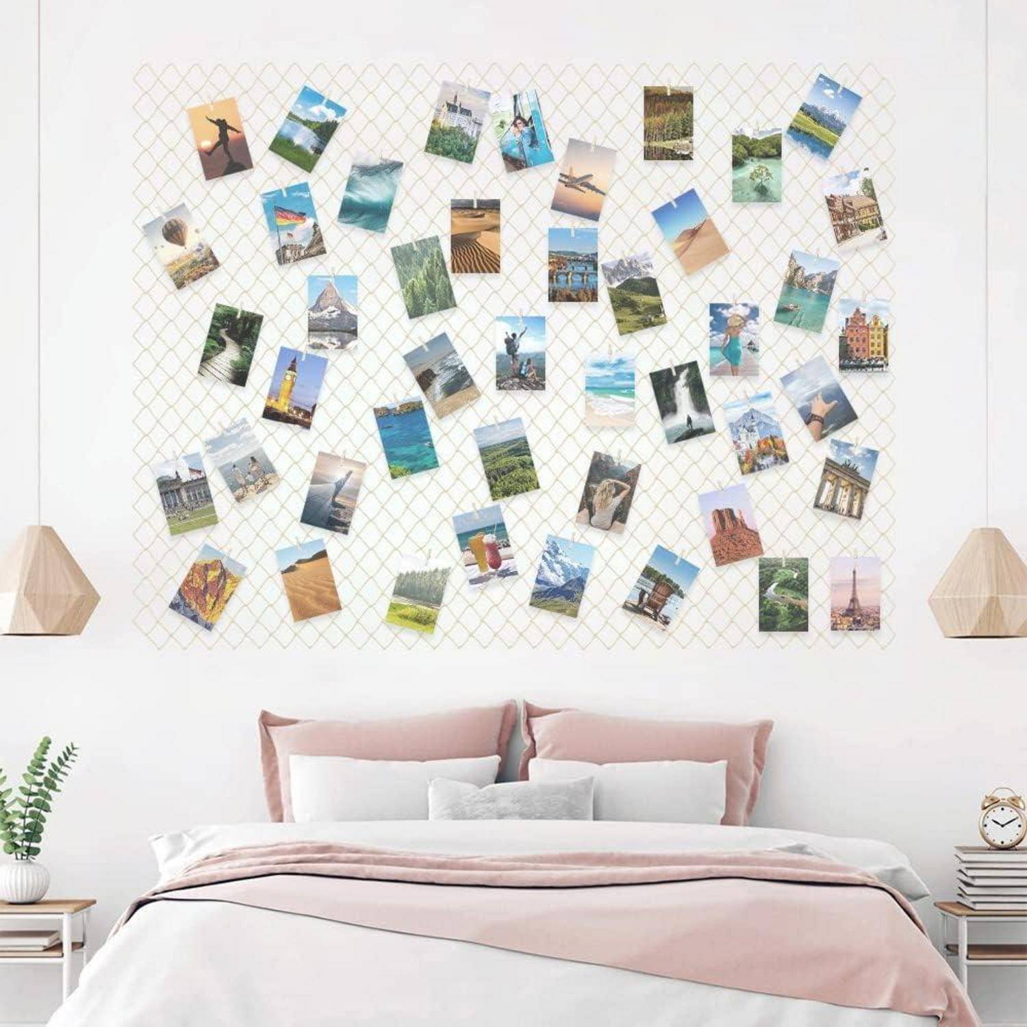 Eine Schlafzimmerwand zeigt ein Raster mit verschiedenen Reisefotos, die daran angeheftet sind. Das Bett darunter hat rosa und weiße Bettwäsche und zwei Holznachtlampen.