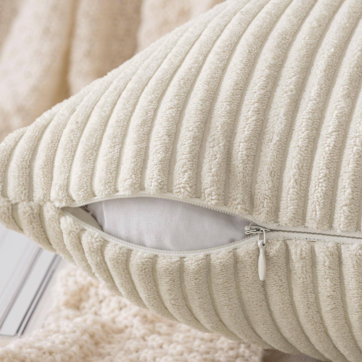 Ein cremefarbenes strukturiertes Kissen mit sichtbarem, teilweise geöffnetem Reißverschluss, der das Innenfutter erkennen lässt. Es ruht auf einer passenden gestrickten Decke.