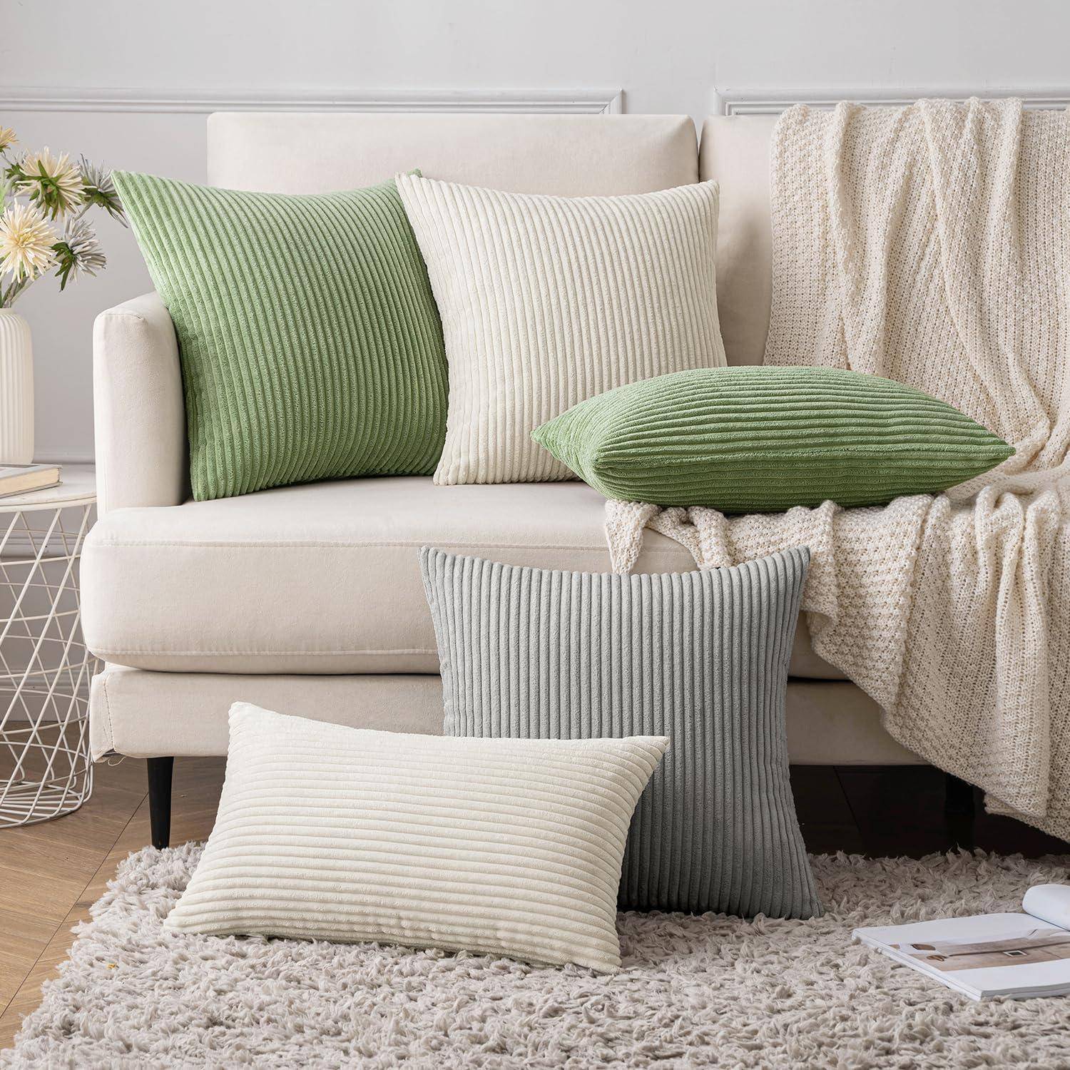 Eine gemütliche Wohnzimmerszene mit einem weißen Sofa, das mit gestreiften Kissen in Grün, Weiß und Grau versehen ist, neben einem Beistelltisch mit einer Pflanze.