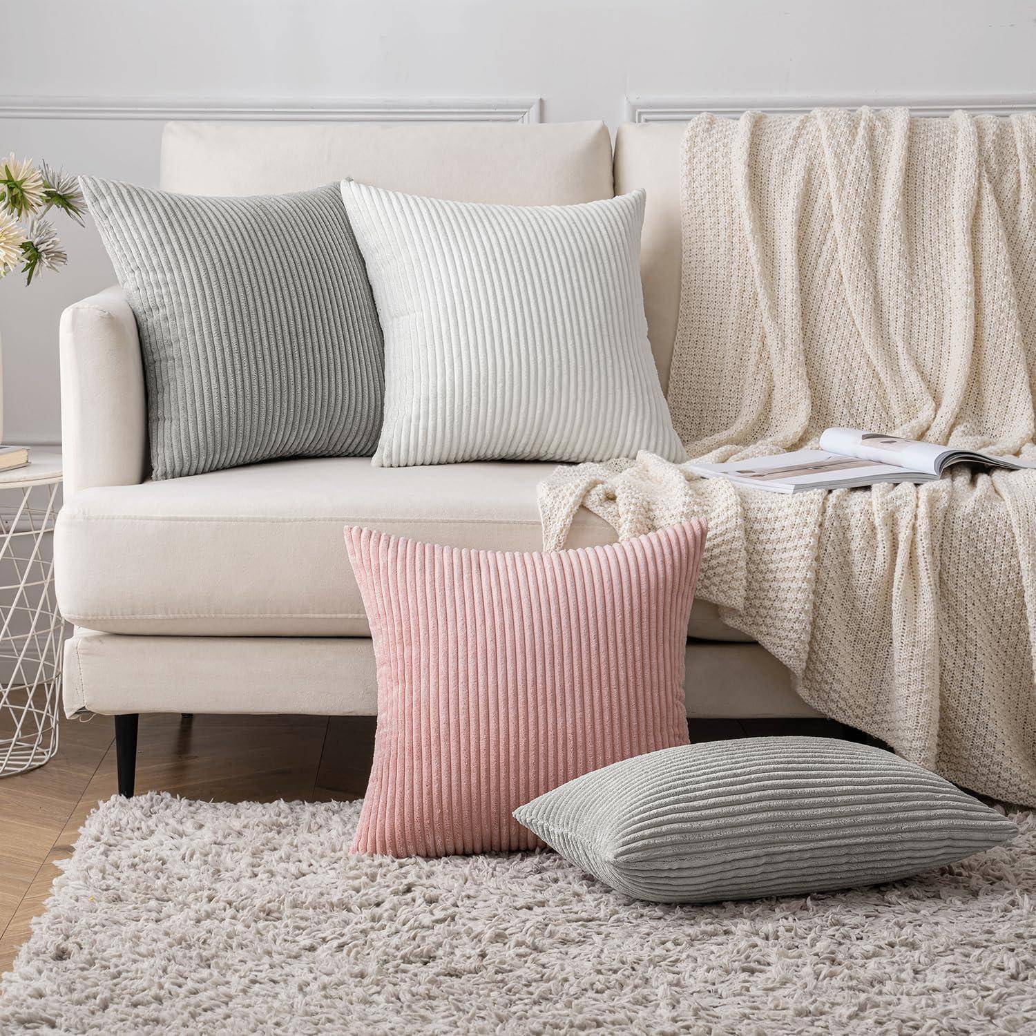 Eine gemütliche Wohnzimmerszene mit einem weißen Sofa, ausgestattet mit zwei großen gerippten Kissen in Grau und einem in Rosa. Eine weiche beige Decke drapiert sich über das Sofa.