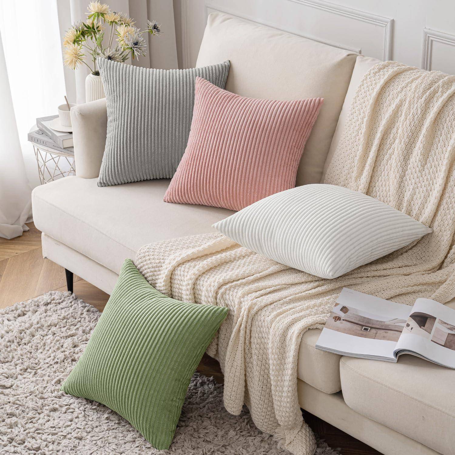 Ein gemütliches Wohnzimmer mit einem cremefarbenen Sofa, das mit vier gerippten Kissen in Grau, Rosa, Weiß und Grün geschmückt ist. Eine weiche Decke ist über das Sofa gelegt.