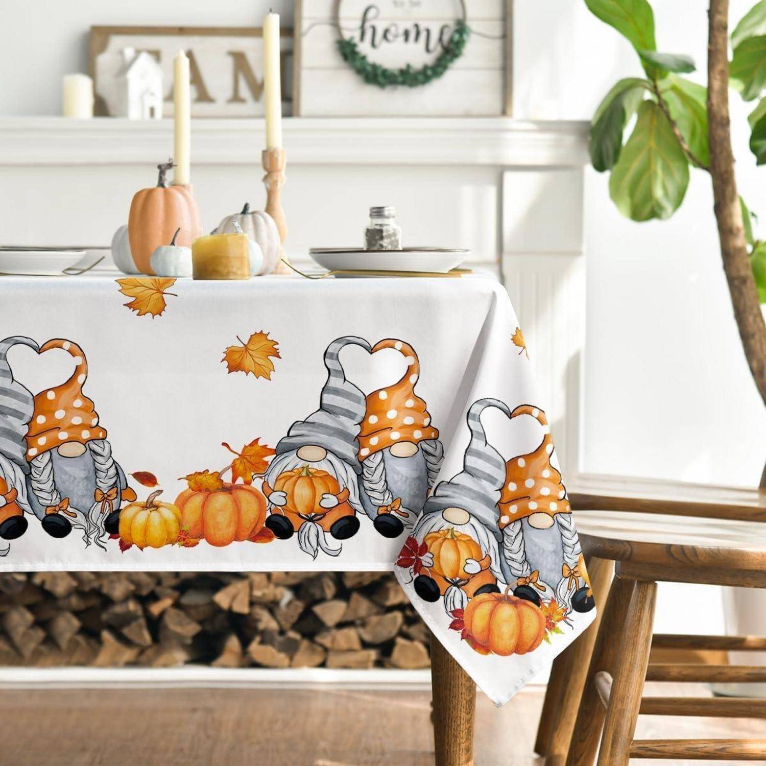 Ein festlich gedeckter Tisch ist mit einer herbstlichen Tischdecke ausgestattet, die Gnome, Kürbisse und Blätter zeigt. Kerzen und kleine Kürbisse schmücken die Dekoration.