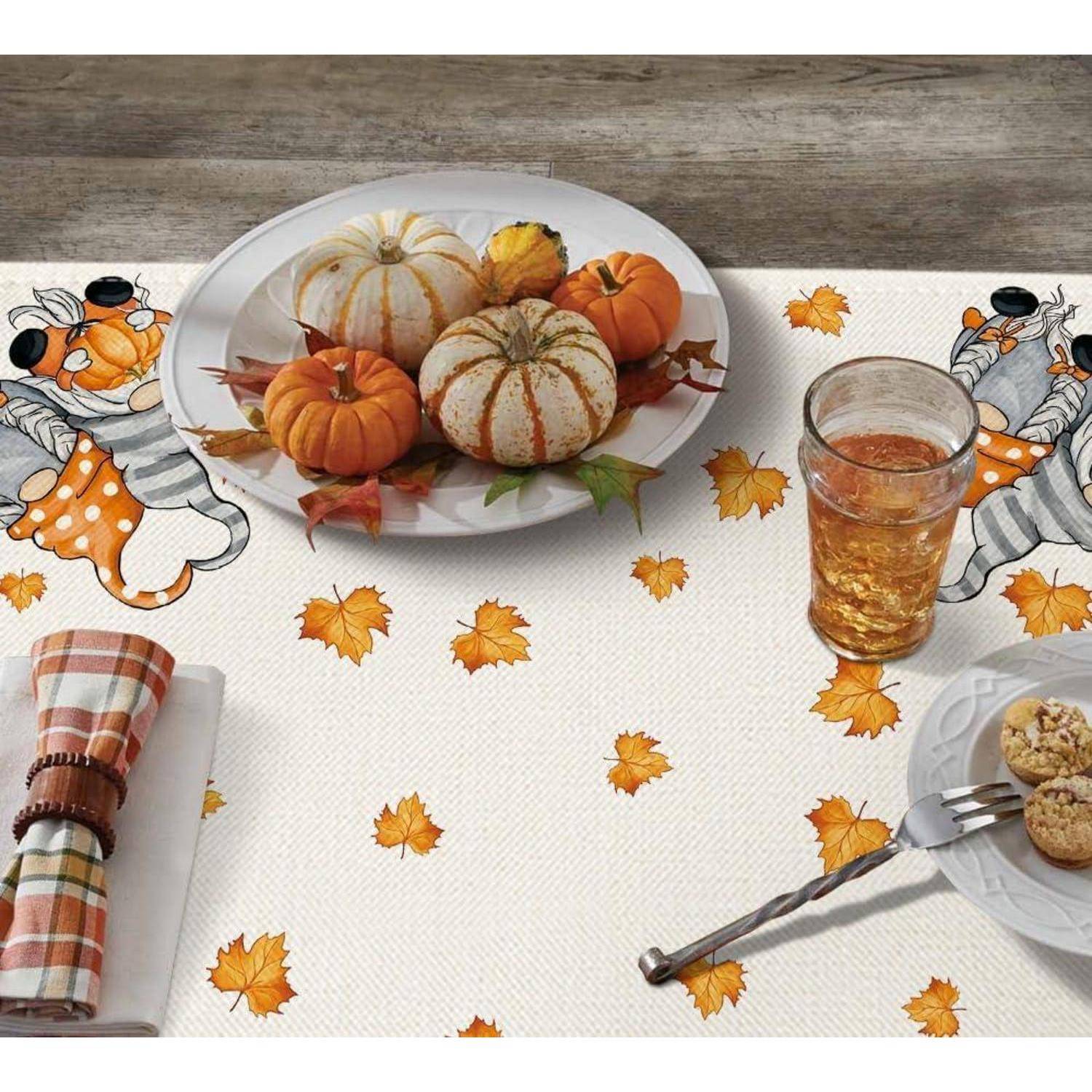 Gedeck mit Herbstmotiv; Kürbisse, Blätter, ein Getränk, Kekse und eine Serviette auf einer Tischdecke mit Cartoon-Katzendesigns.