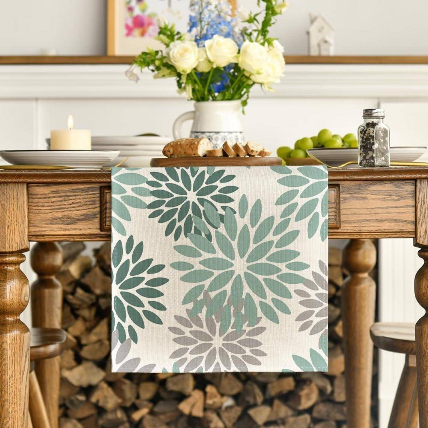 Ein Holz-Esstisch mit einem blumenmustrigen Tischläufer, darauf eine brennende Kerze und eine Vase mit weißen und blauen Blumen, aufgestellt in einem gemütlichen Raum.