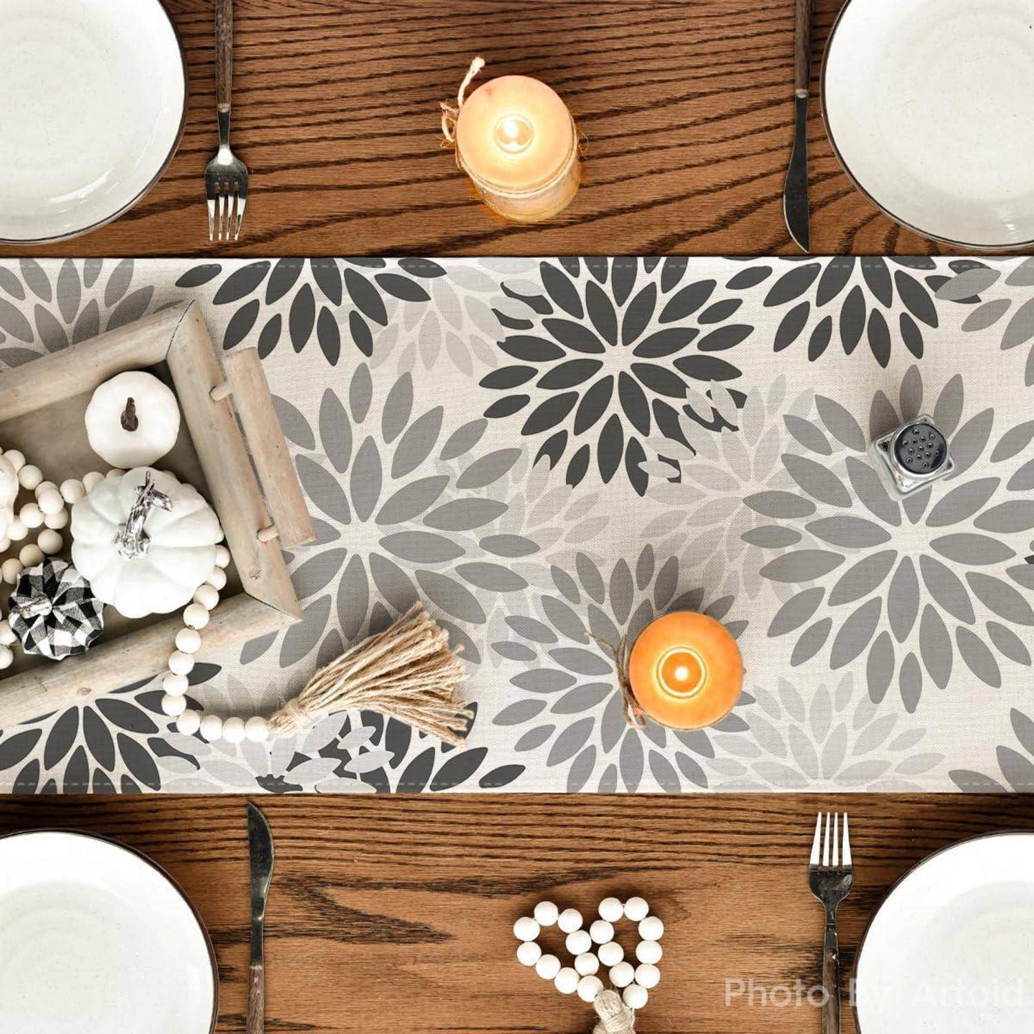 Eine Tischdecke mit einem Läufer mit Blumenmuster, Kerzen und dekorativen Gegenständen auf einem Tablett. Teller, Gabeln und ein Serviettenring vervollständigen die Tischdekoration.