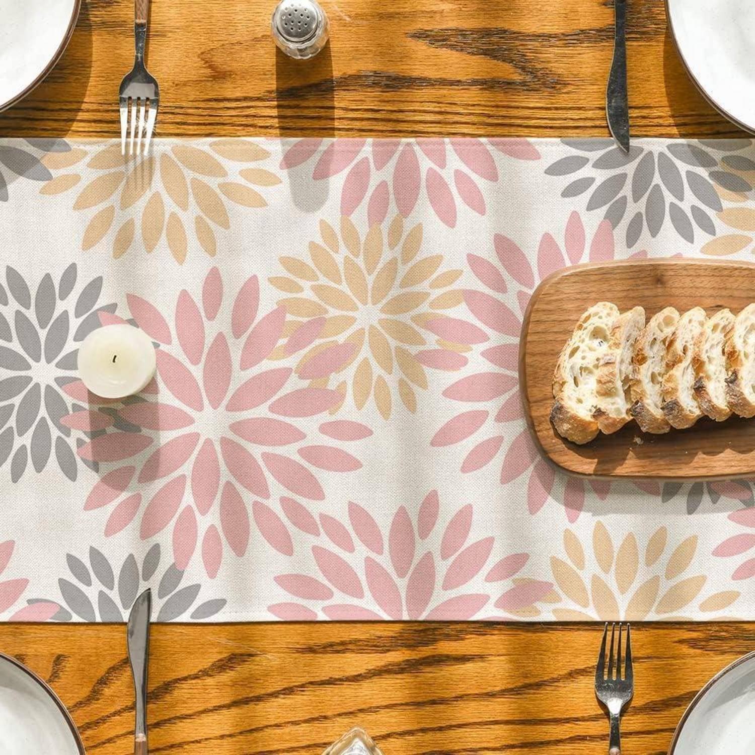 Ein Tischgedeck mit einem blumenmusterigen Tischläufer, Gabeln und Messern, einer Kerze, einem Pfefferstreuer und einem Holzbrett mit aufgeschnittenem Brot.