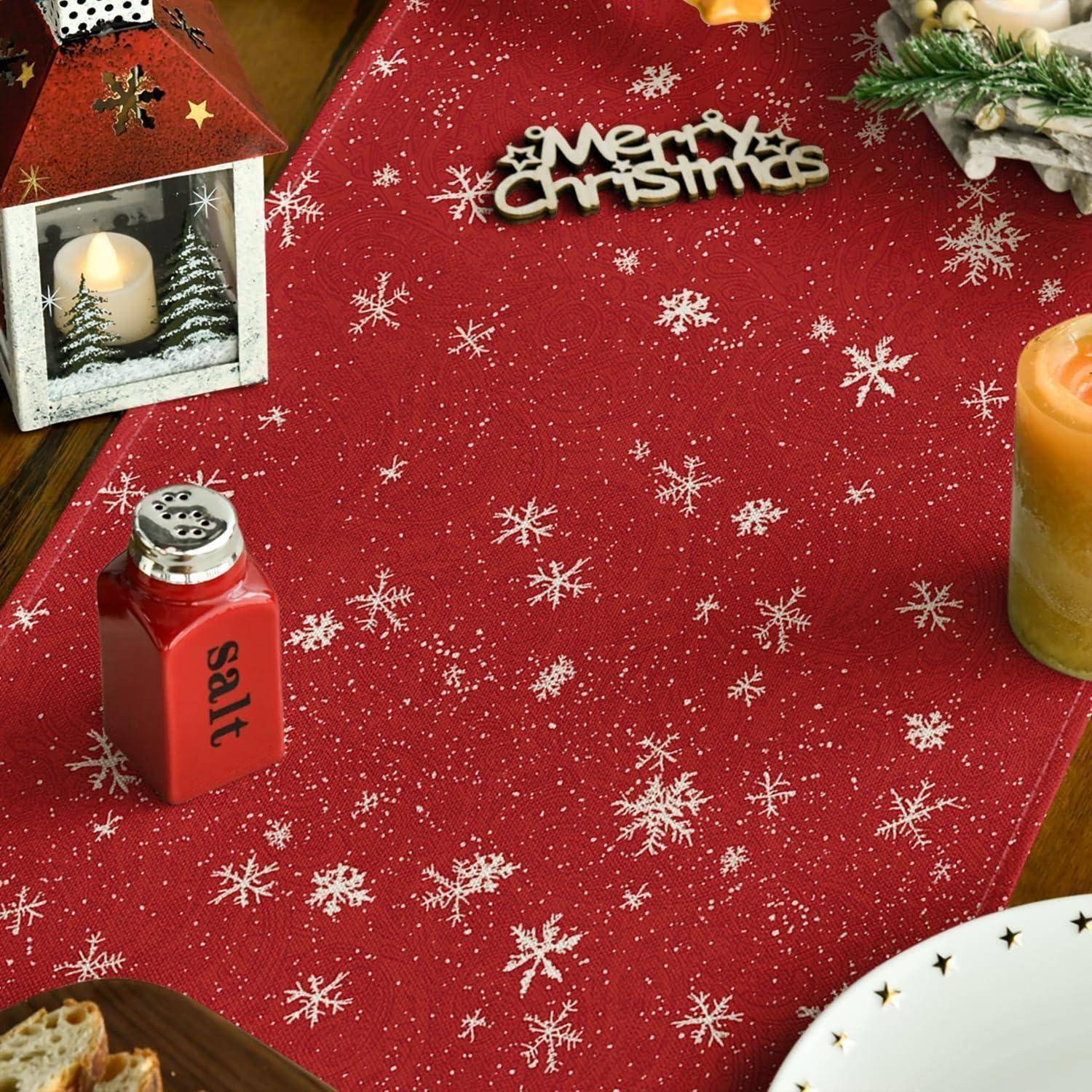 Ein festlich gedeckter Tisch mit einem roten Tuch mit Schneeflockenmuster, einer Kerze in einem hausförmigen Kerzenhalter, einem Salzstreuer und Weihnachtsdekoration mit der Aufschrift 