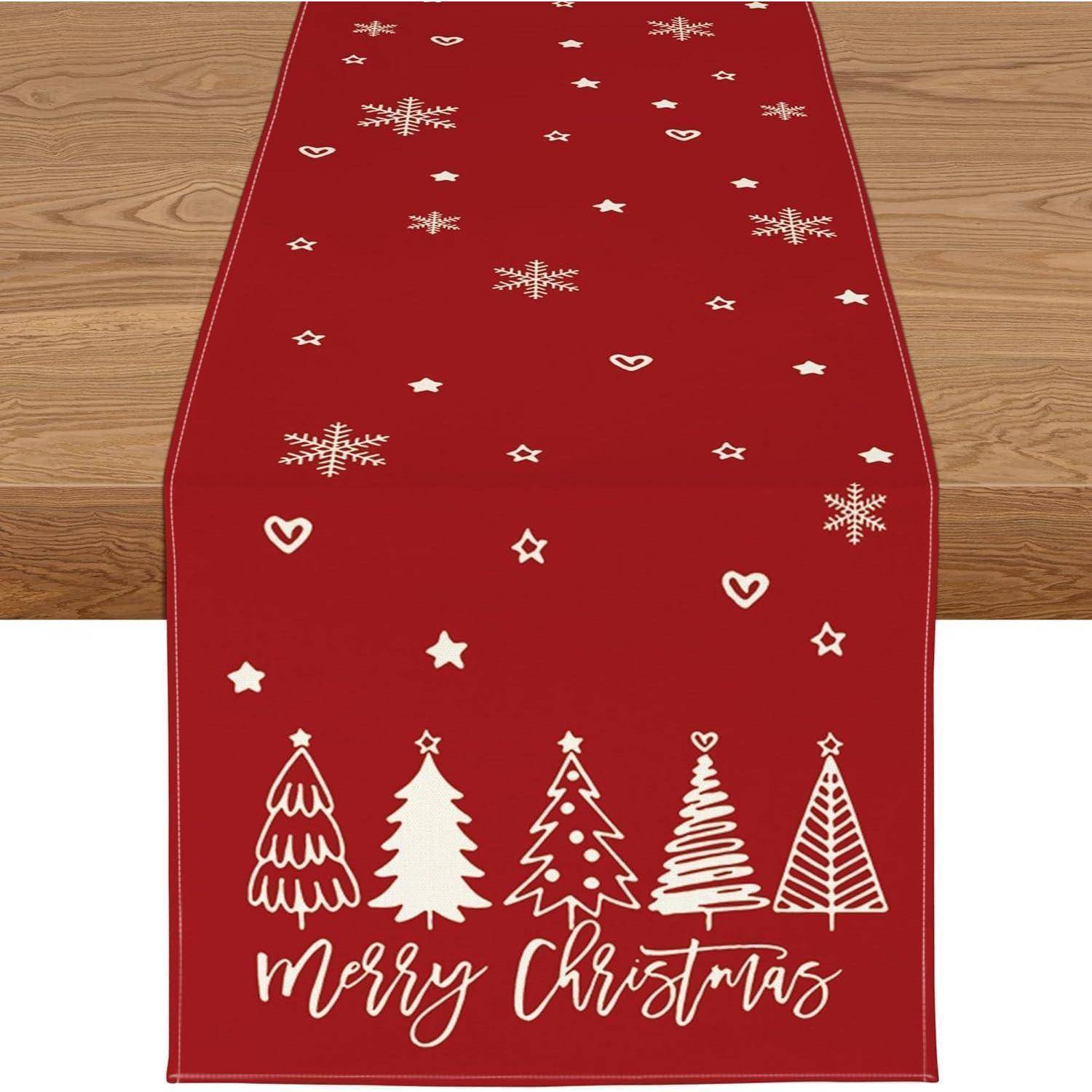 Roter Tischläufer mit weißen Schneeflocken, Sternen, Herzen und Weihnachtsbäumen. Die Worte 'Frohe Weihnachten' sind in weißer Schrift geschrieben.
