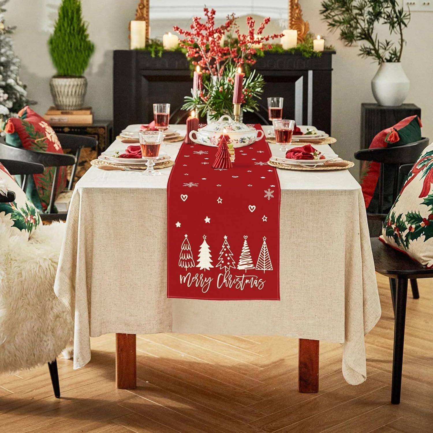 Festlich gedeckter Esstisch mit Weihnachtsmotiv, der einen roten Läufer mit Baumdesigns und dem Text ‚Frohe Weihnachten' trägt, umgeben von Dekorationen.