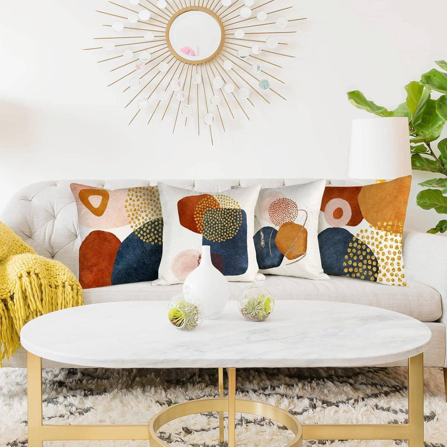 Ein modernes Wohnzimmer mit einem weißen Sofa, geschmückt mit bunten geometrisch gemusterten Kissen, einem runden Marmor-Couchtisch und einem Sonnenspiegel.