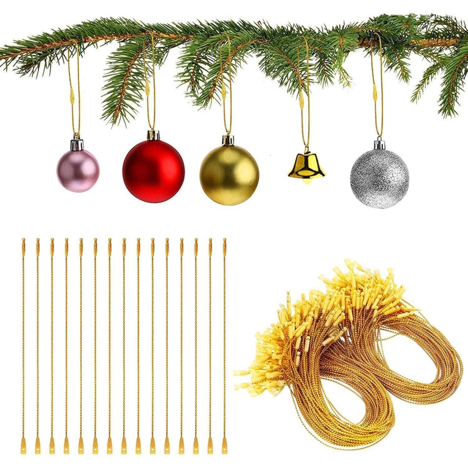 Ein Tannenzweig mit roten, goldenen, silbernen und rosa Christbaumkugeln und einer Glocke, die daran hängt. Darunter befinden sich goldene Baumschmuckhaken und zusammengerollte Schnüre.