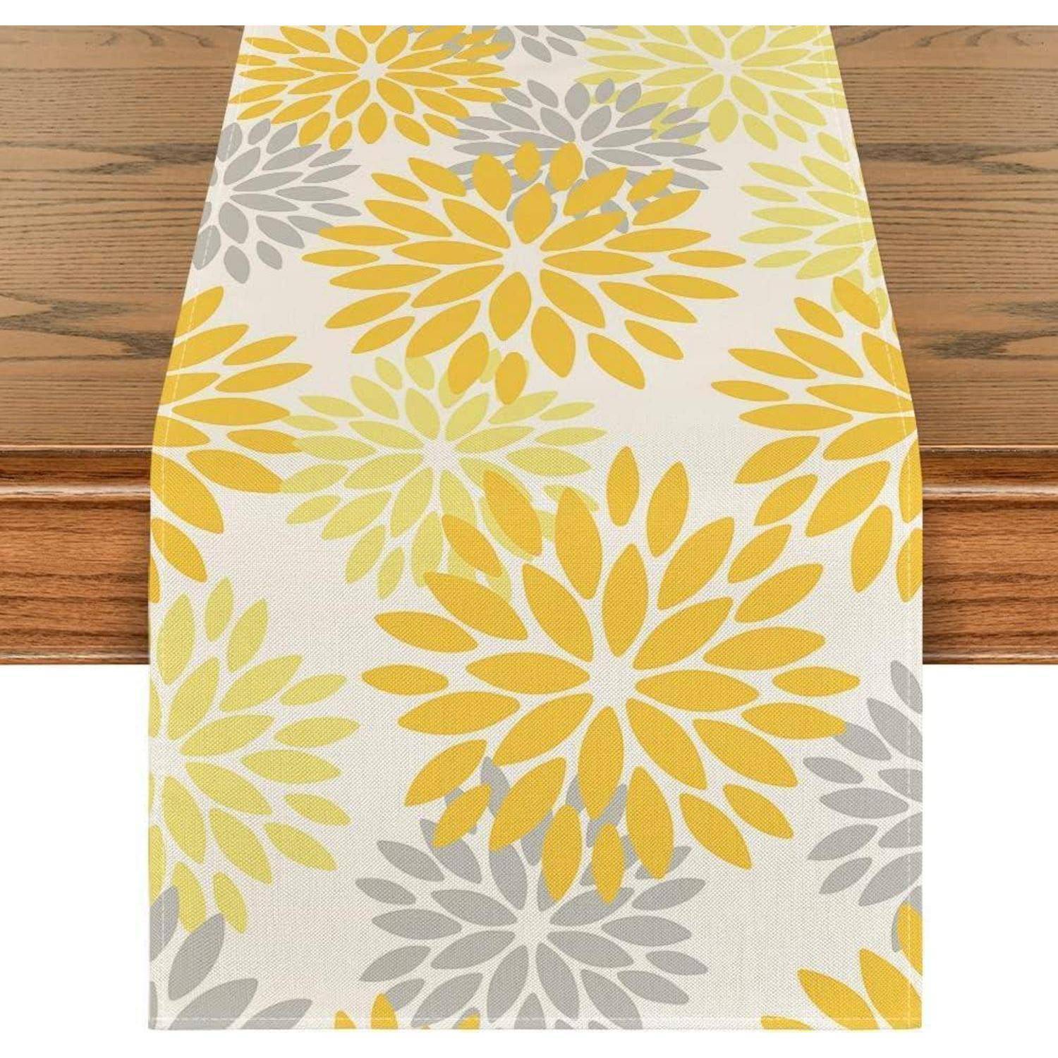 Tischläufer mit Blumenmuster in Gelb, Grau und Hellgrün, auf einem Holztisch präsentiert.