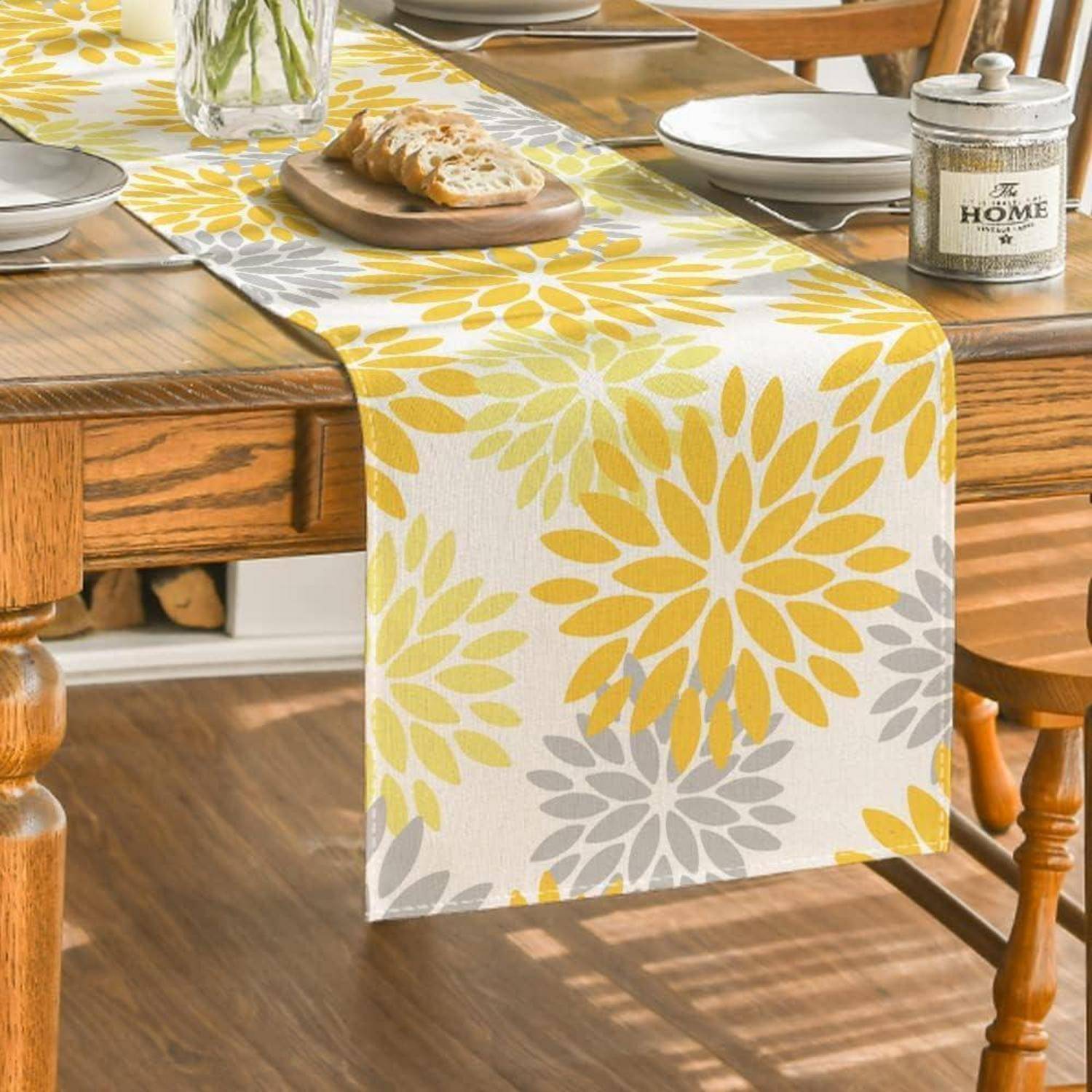 Gelb-grauer Blumenläufer auf einem Holzesstisch, mit Tellern, Brot und einem Glas mit der Aufschrift „Selbstgemacht