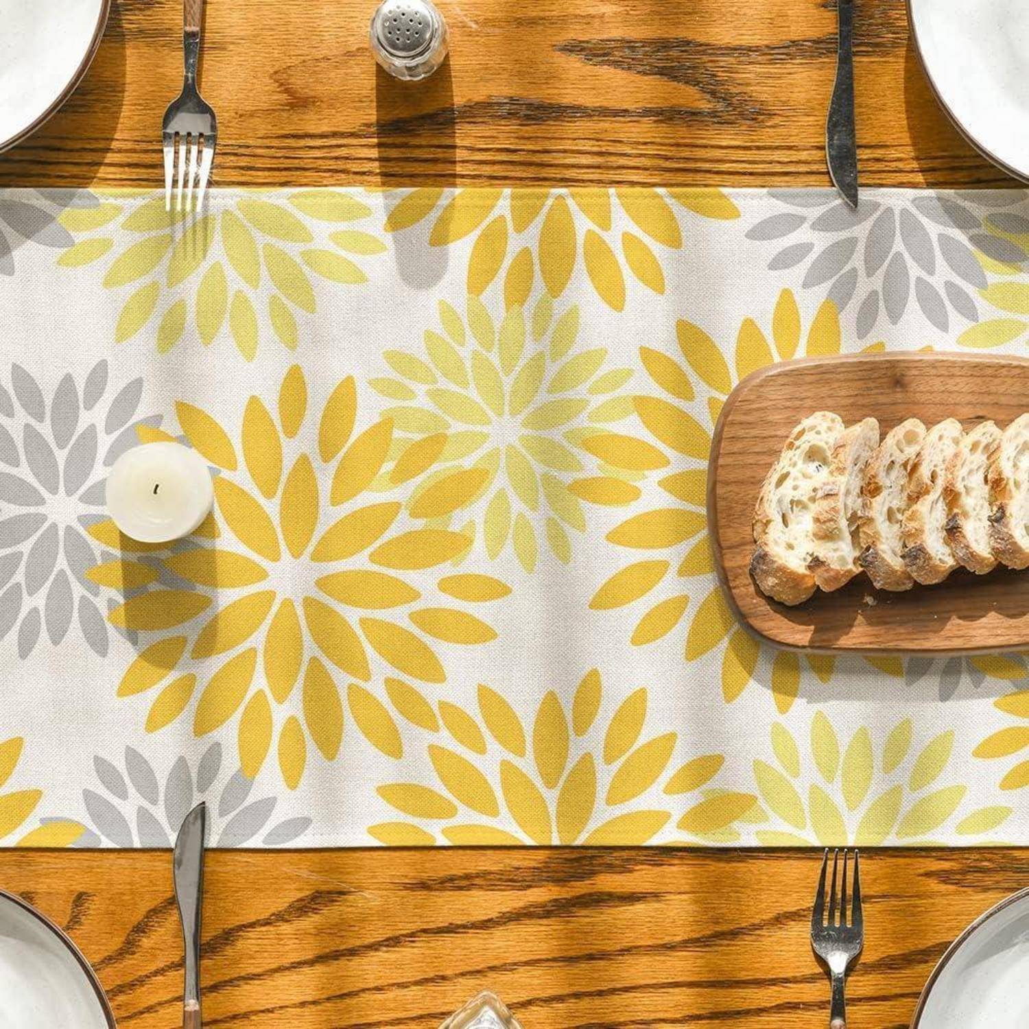 Ein Holztisch, gedeckt für eine Mahlzeit, mit einem Tischläufer mit Blumenmuster, Silberbesteck, einer Kerze und einem Schneidebrett mit aufgeschnittenem Brot.