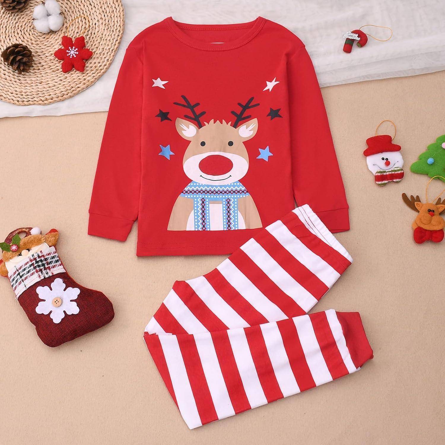 Rote Kinderpyjamas mit einem Rentiermotiv, kombiniert mit rot-weiß gestreiften Hosen. Umgeben von weihnachtlichen Dekorationen.