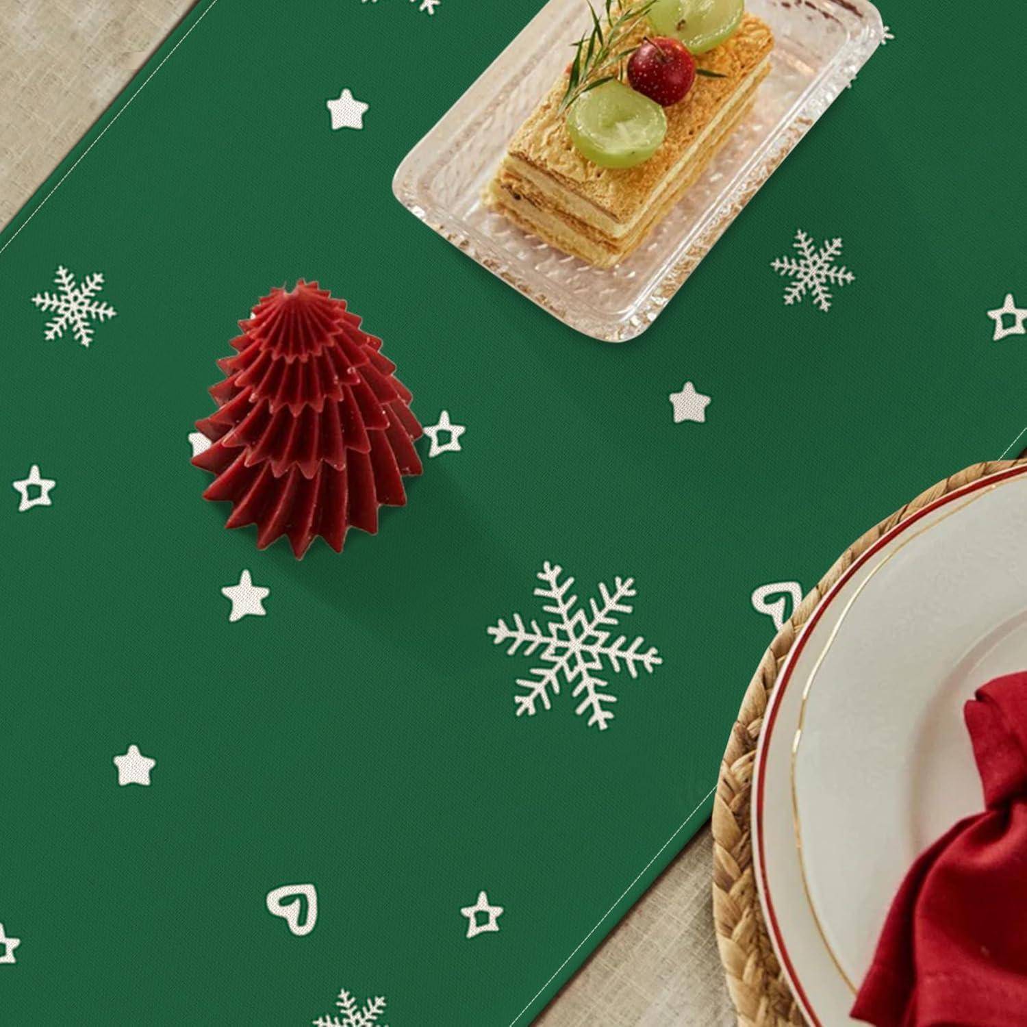 Eine festliche Tischdekoration mit roter Serviette, dekoratives grünes Tischset mit Schneeflocken und Sternen, Kuchenplatte mit Pistazie und Kirsche als Topping.