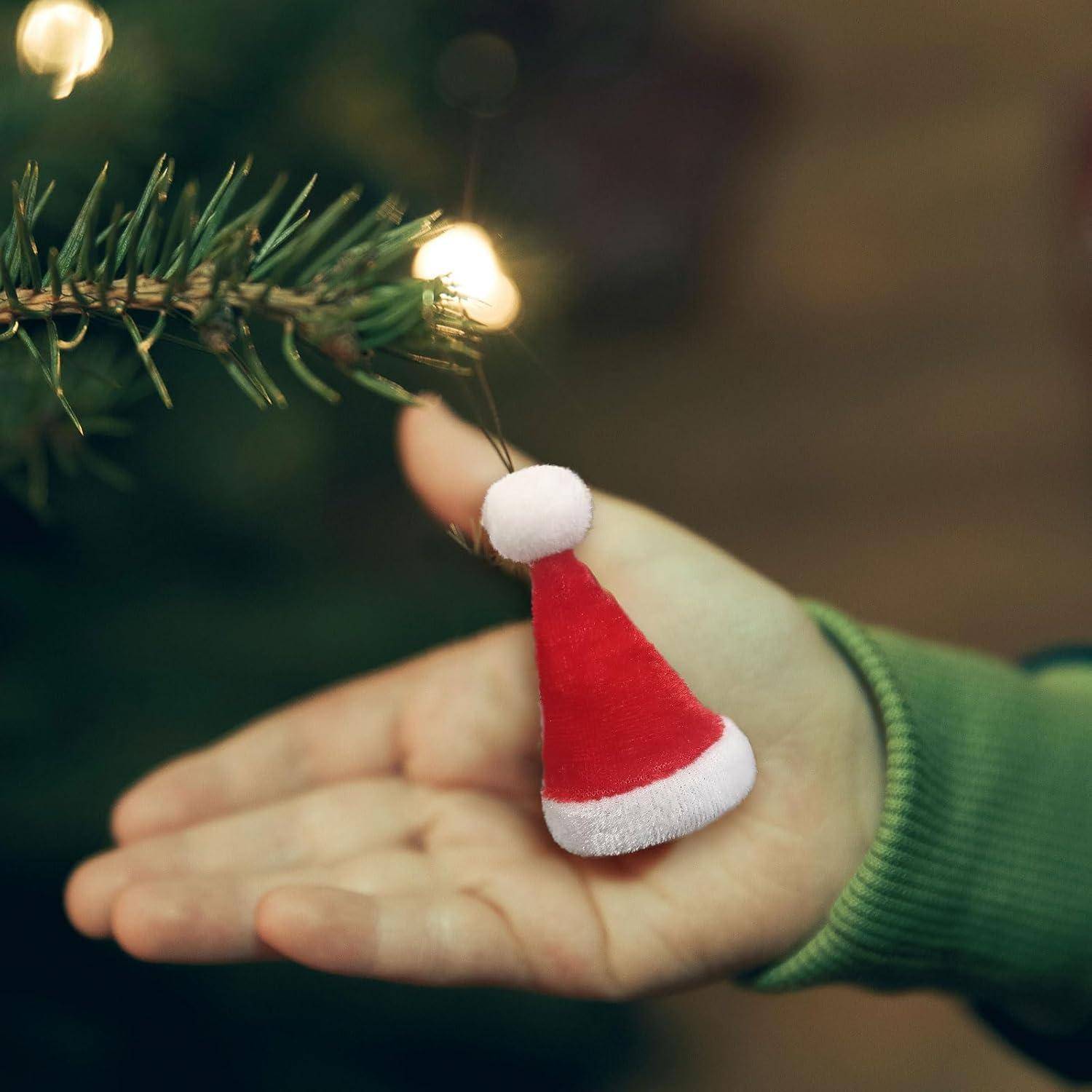Eine Hand hält eine kleine rot-weiße Weihnachtsmannmütze als Christbaumschmuck neben einem beleuchteten Weihnachtsbaumzweig und vermittelt eine festliche Weihnachtsstimmung.